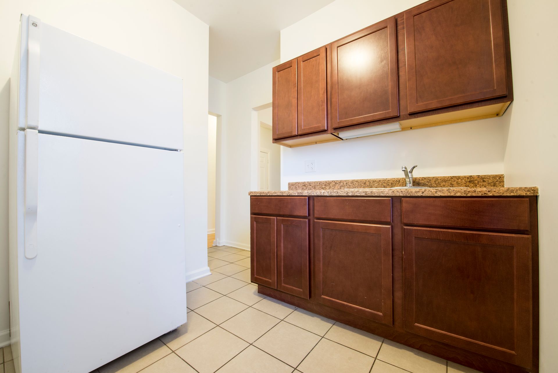 Kitchen with white refrigerator, brown cabinets, and tan countertop; tiled floor.