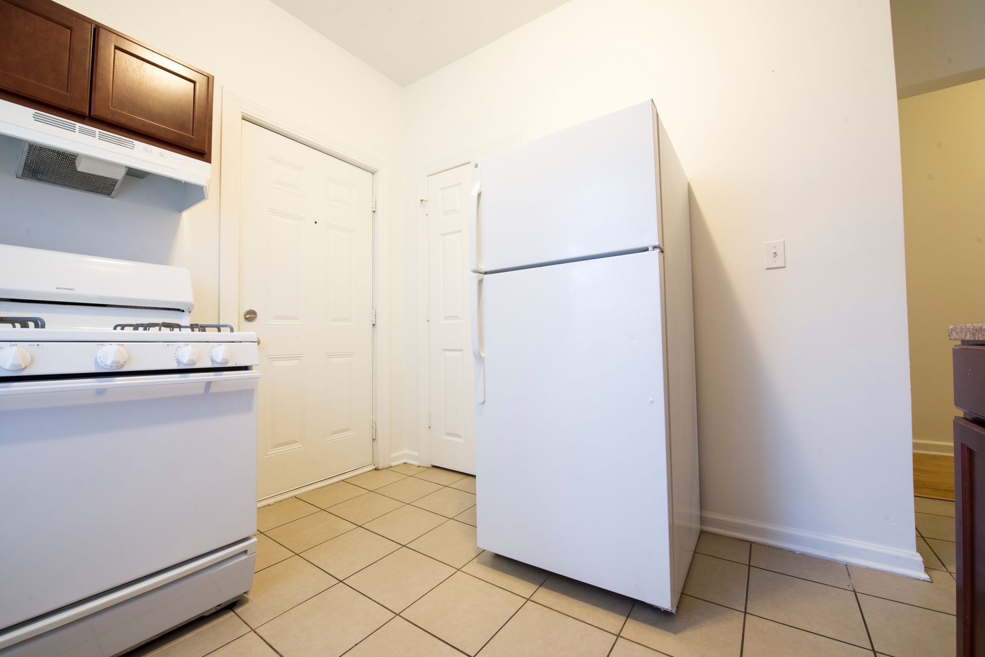 Kitchen with a white refrigerator, stove, and tile flooring. A closed white door is in the background.