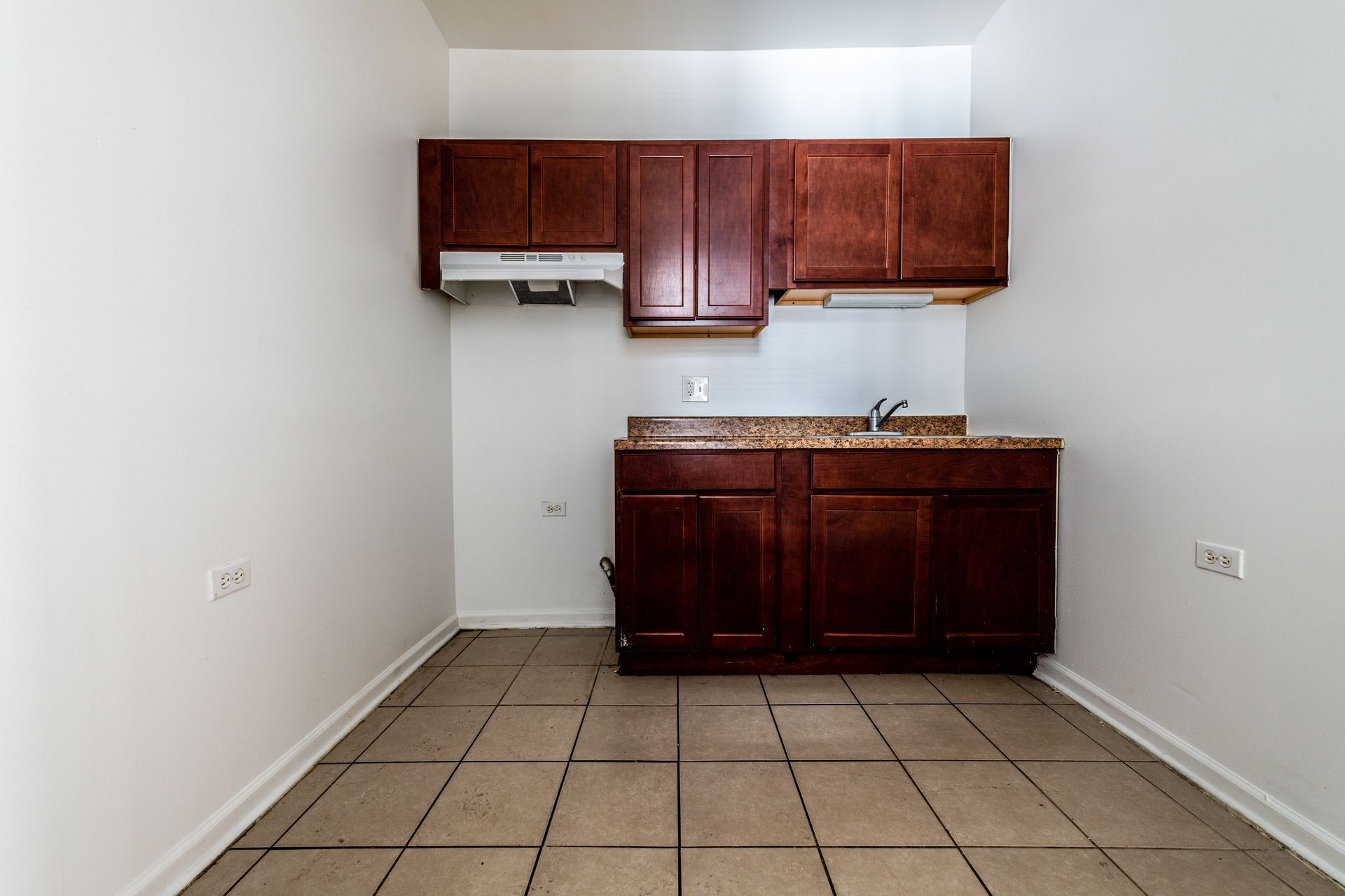 Small kitchen with dark brown cabinets, a sink, and a range hood. The floor is tiled.