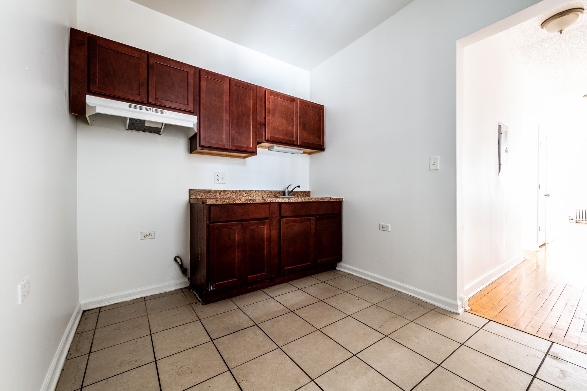 Empty kitchen with dark brown cabinets, a sink, and tiled floor.