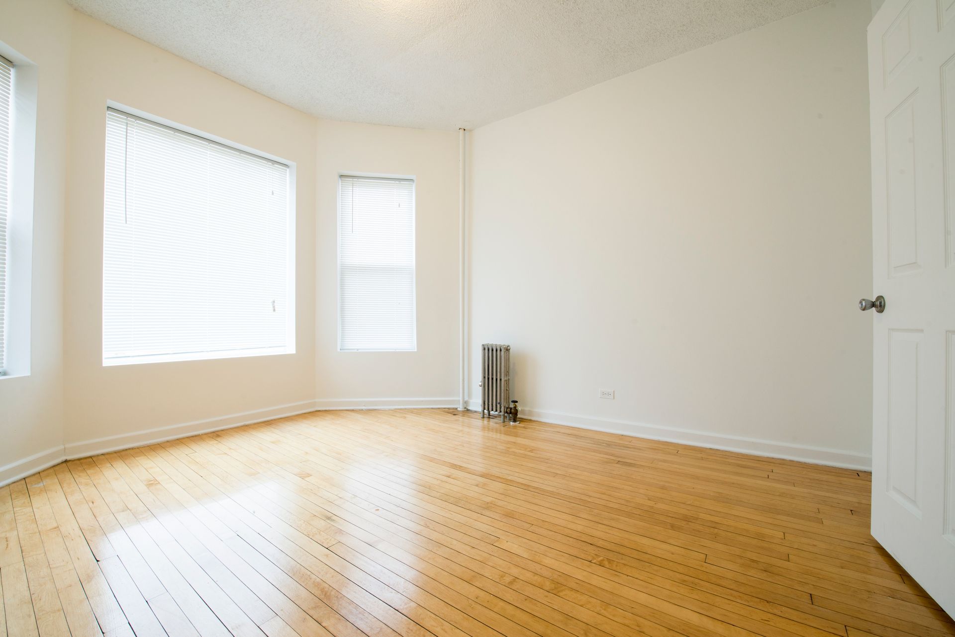 Empty room with hardwood floors, white walls, and three windows with blinds.
