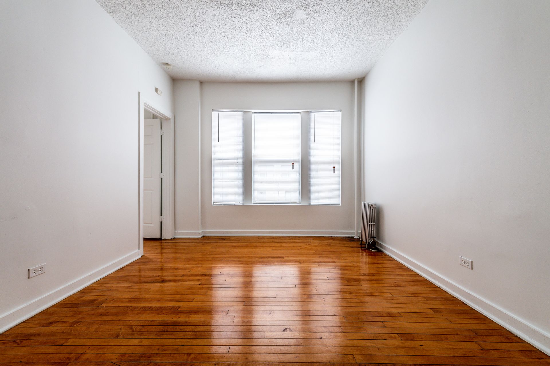 Empty room with hardwood floors, white walls, and a window.