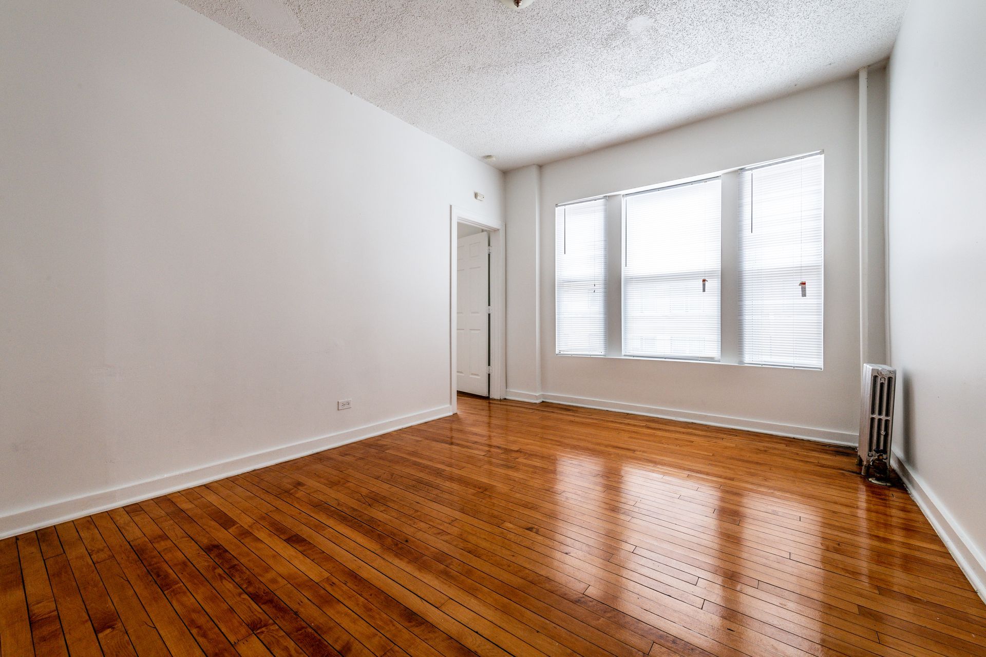Empty room with hardwood floors, white walls, and a window with blinds.