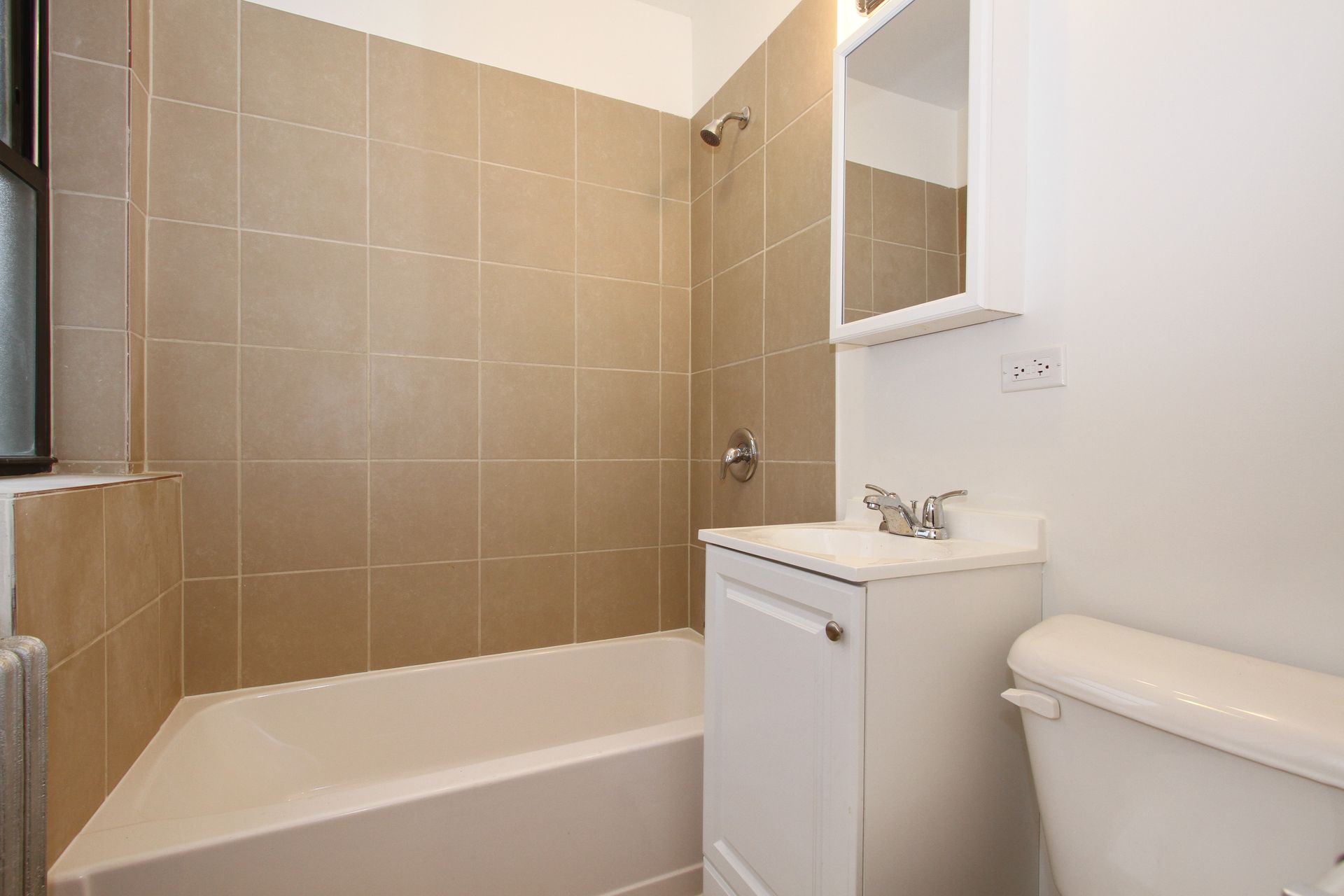 Small bathroom with a white tub, toilet, and vanity, and tan tiled walls.