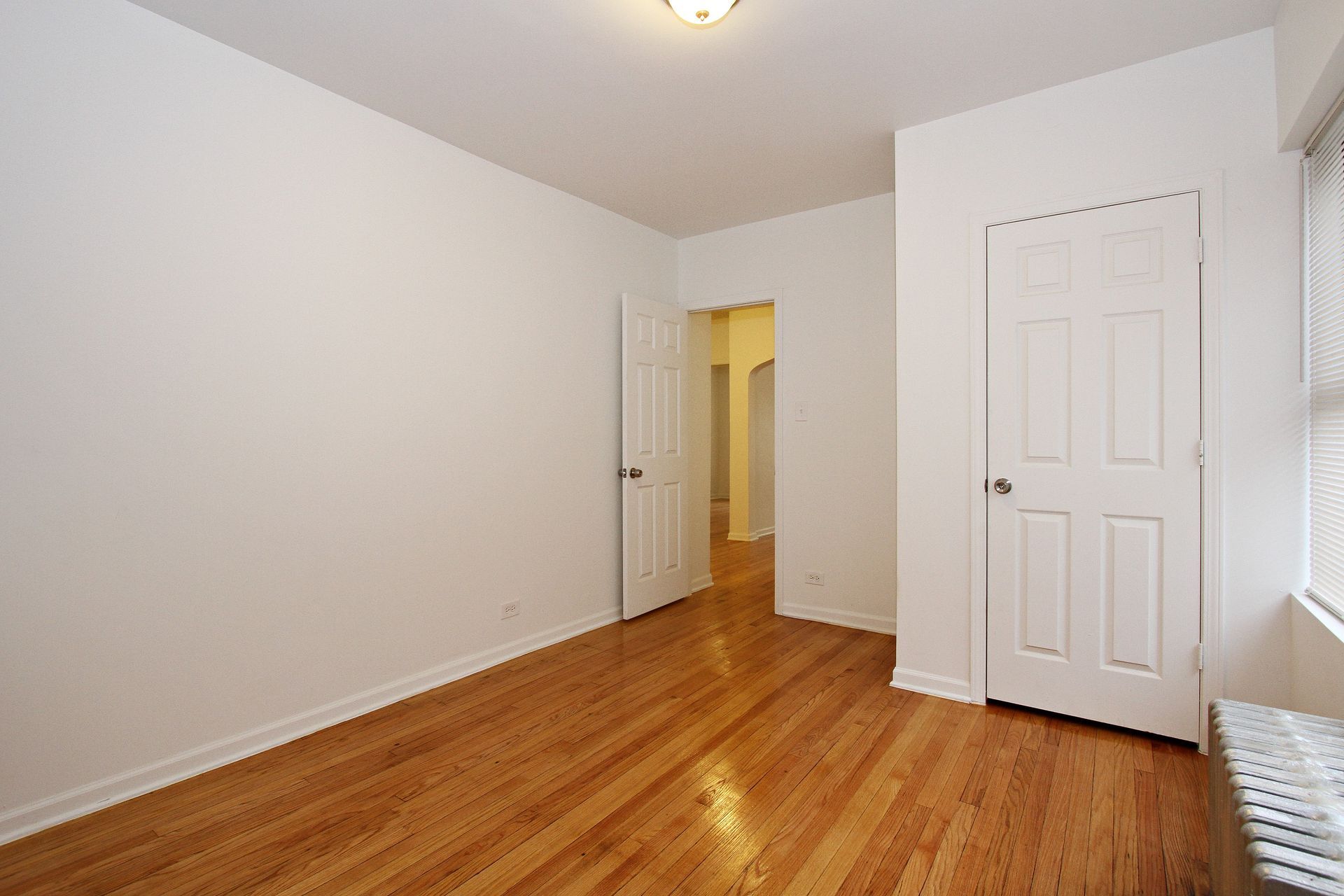 Empty room with hardwood floors, white walls, and two closed doors.