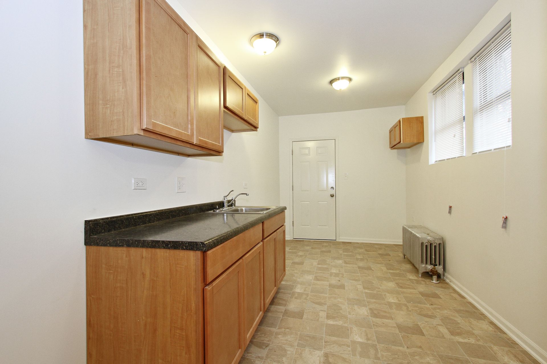 Kitchen with light brown cabinets, dark countertop, sink, and window, and white walls.