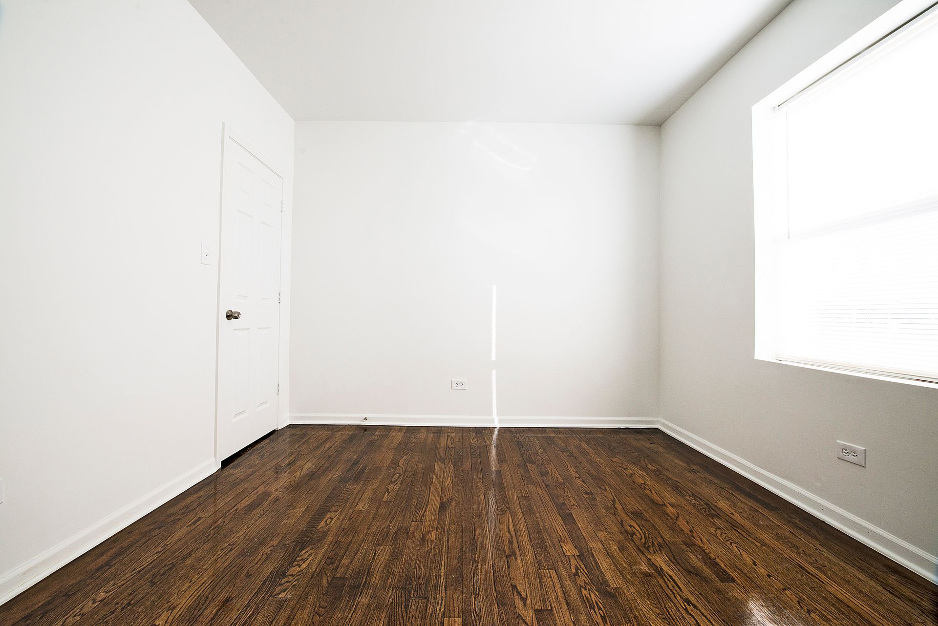 Empty room with dark wood floor, white walls, door, and window.