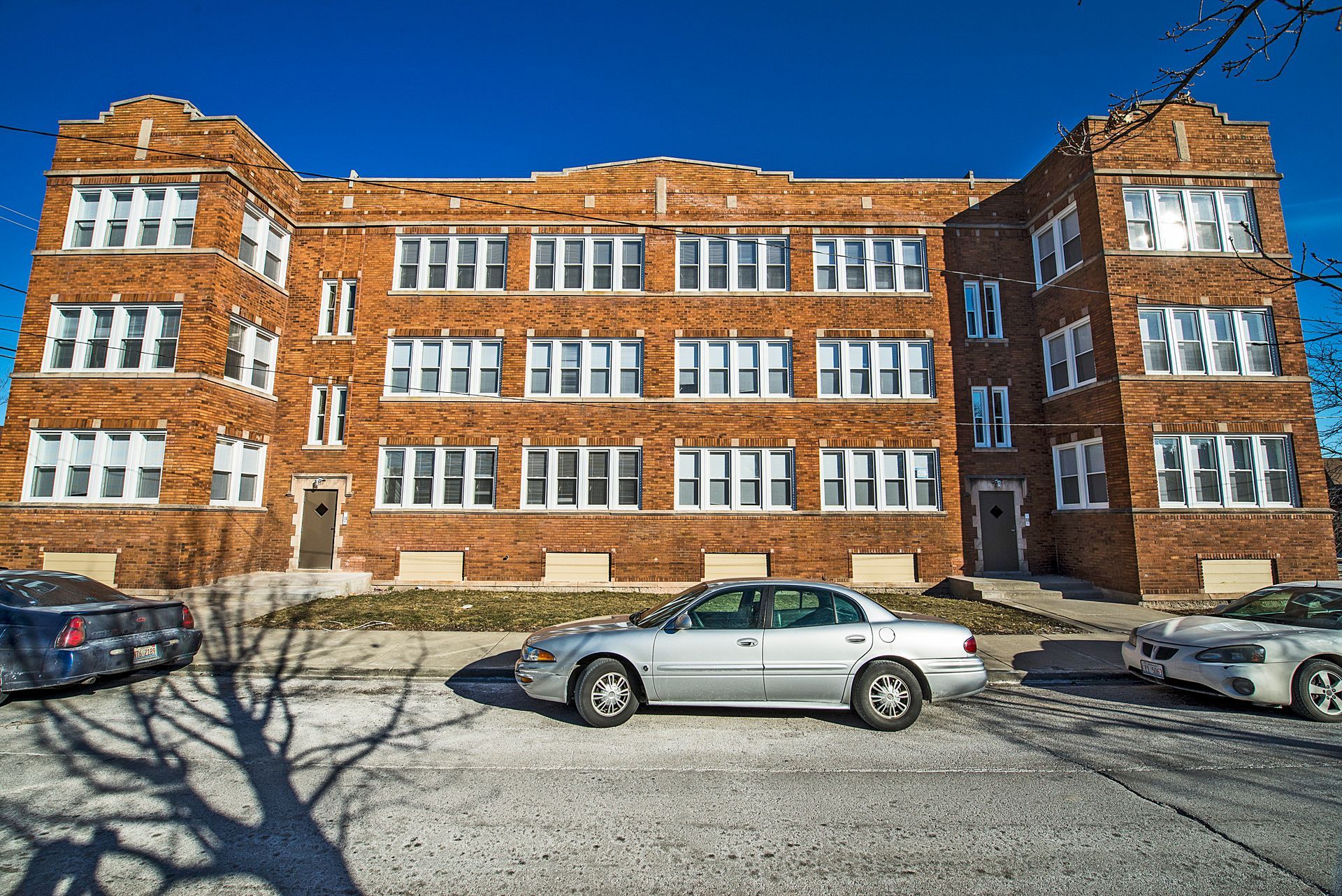 Brick apartment building with parked cars on a sunny day.