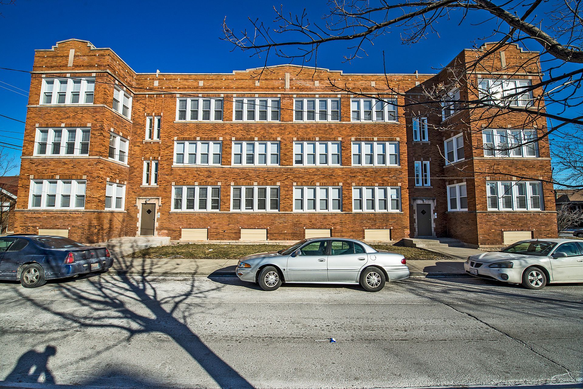 Brick apartment building with parked cars on a sunny day.