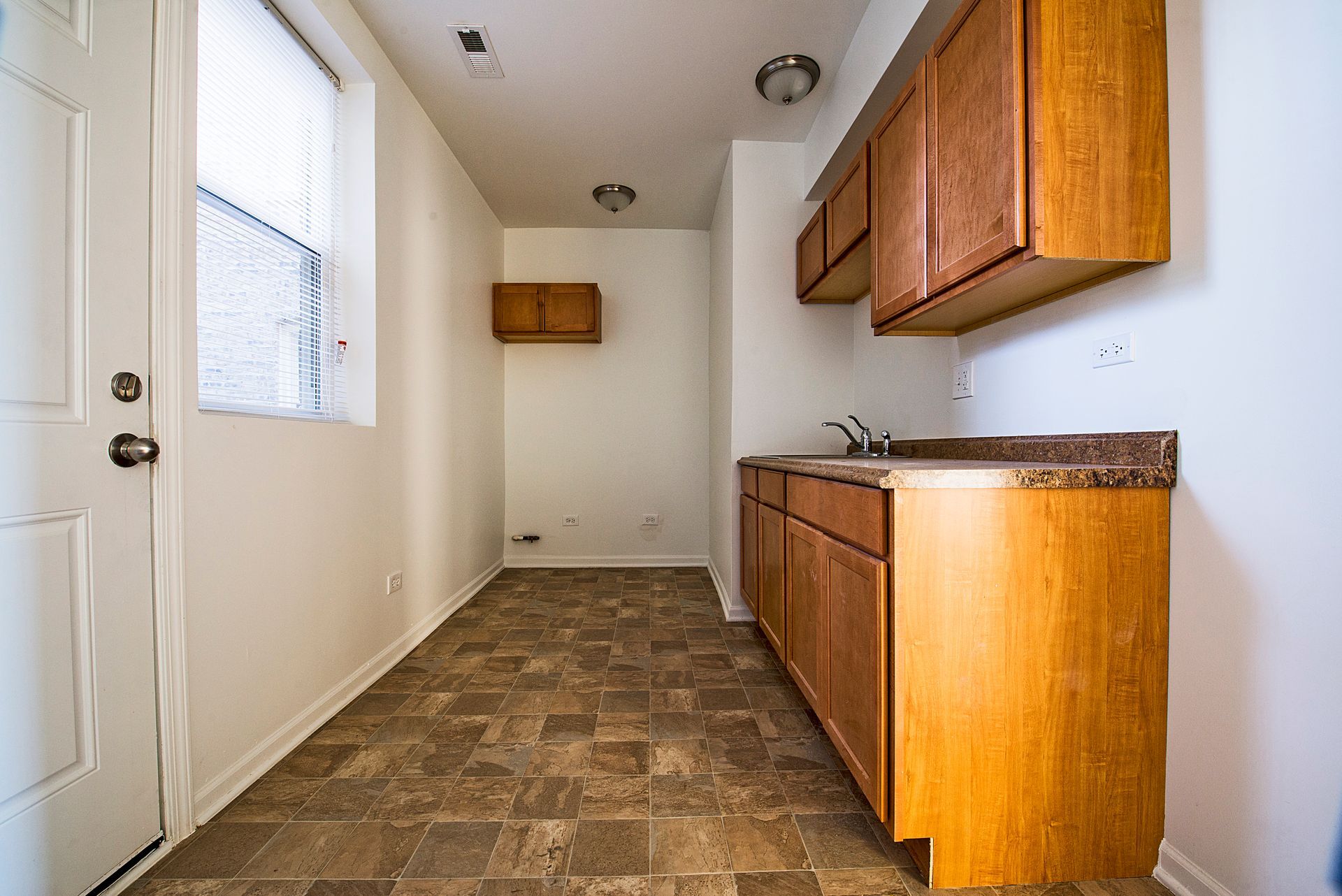 Small kitchen with brown cabinets, sink, window, and door.