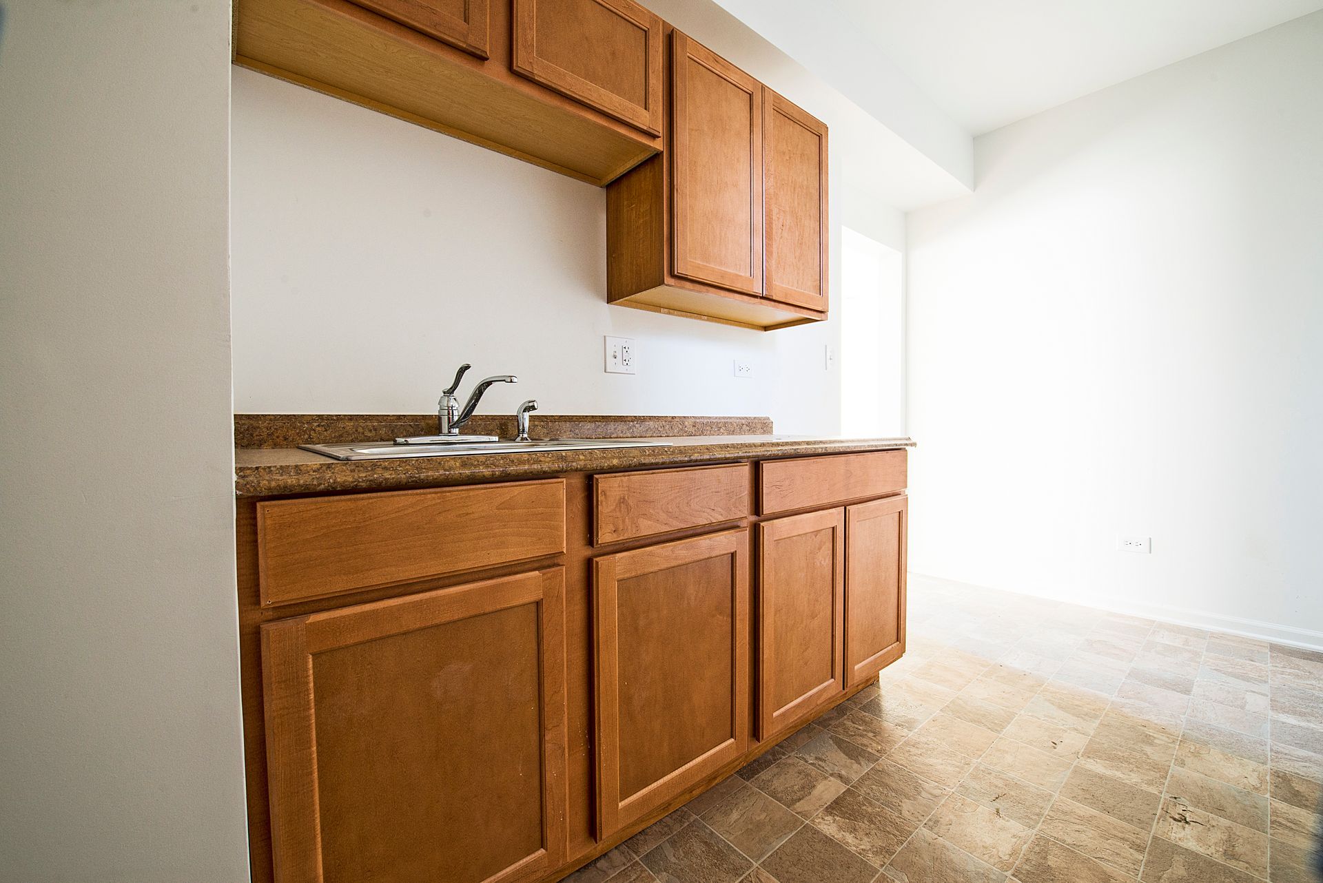 Kitchen with brown cabinets, a sink, and white walls. Brown countertops, beige tile floor.
