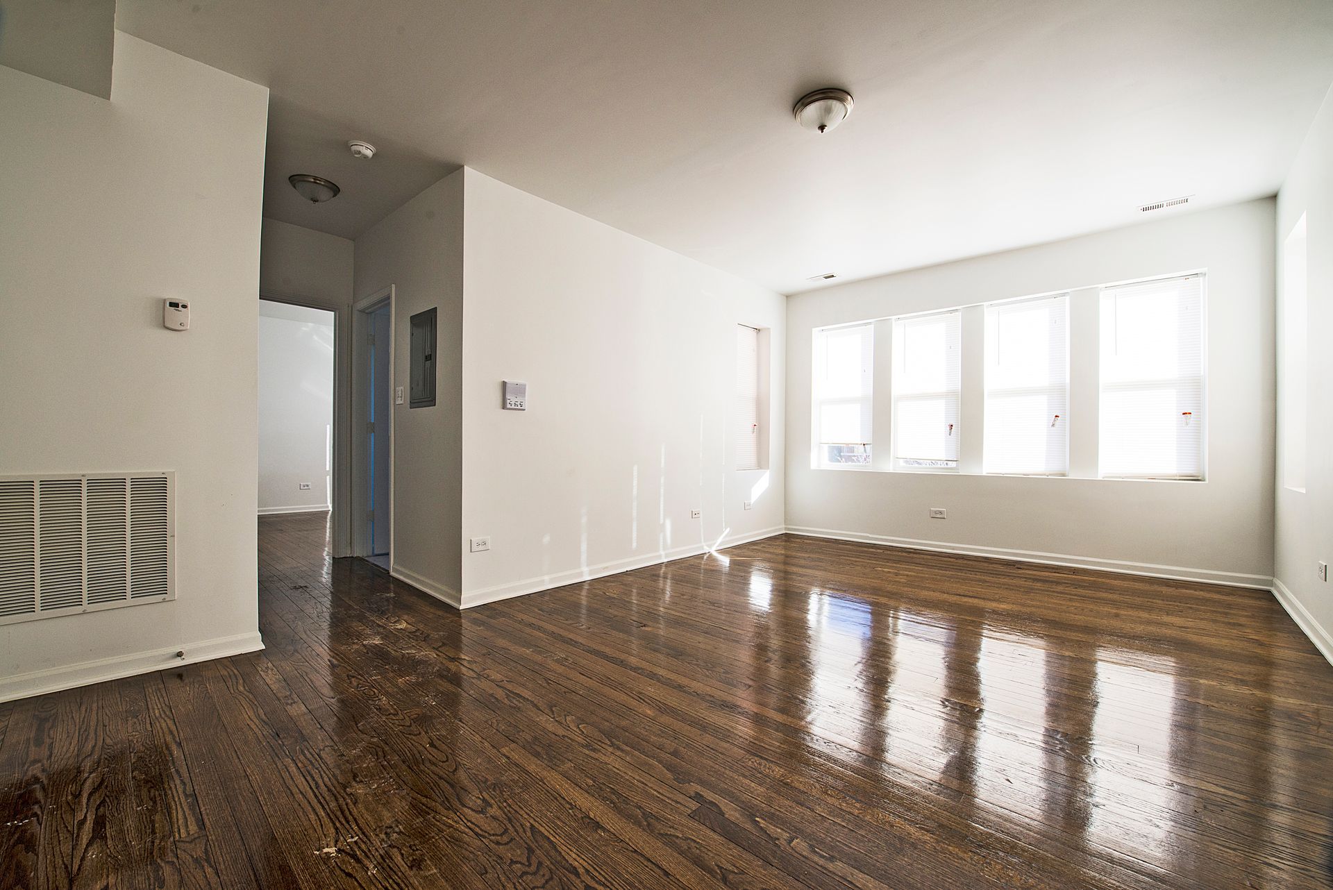 Empty room with glossy wood floors, white walls, and large windows.