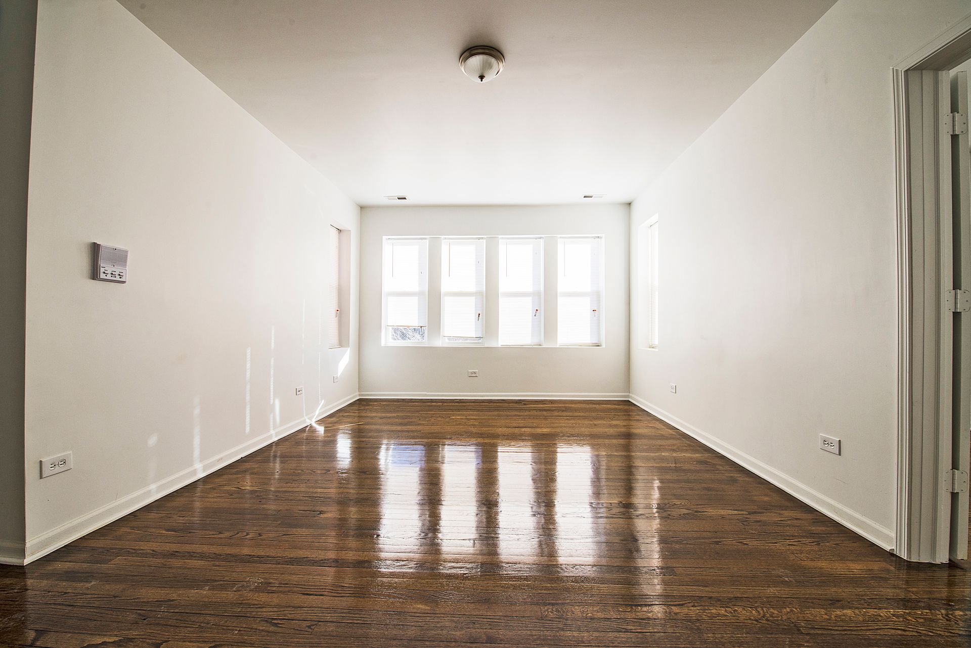Empty room with hardwood floors, white walls, and bright windows.