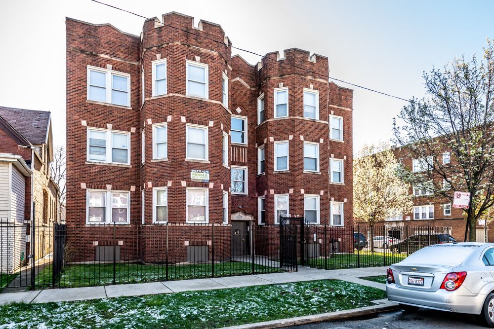 Brick apartment building with decorative turrets and wrought iron fence. A car is parked on the street.