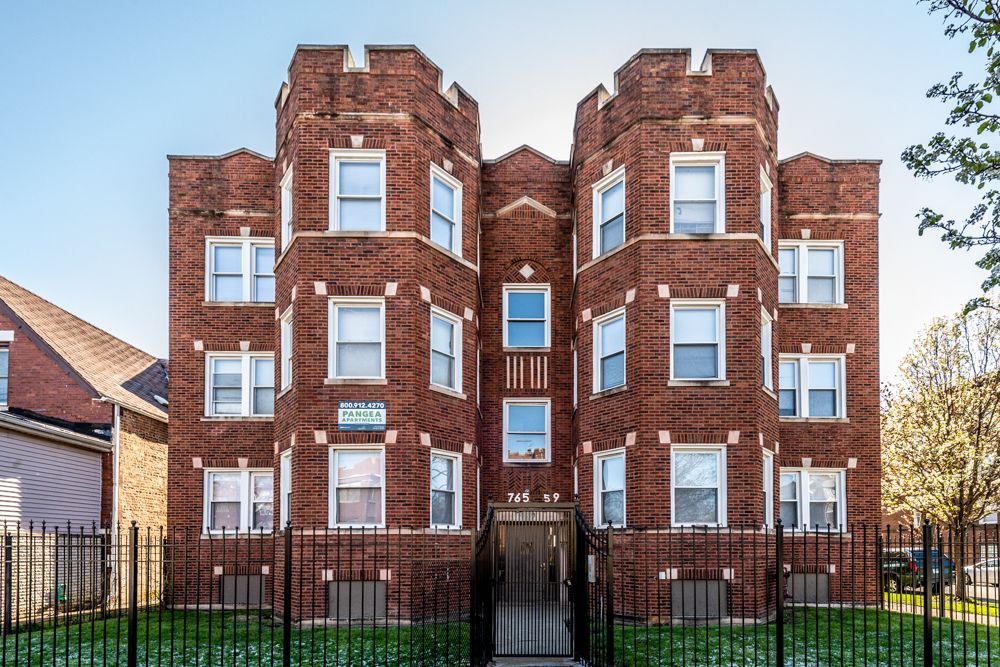 Brick apartment building with decorative turrets and windows, behind a black fence.