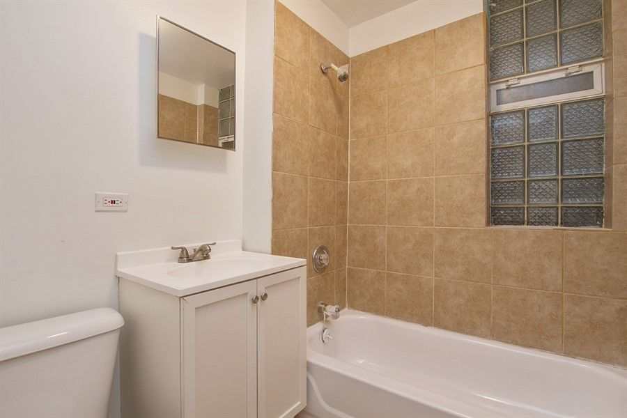 Bathroom with white fixtures, tan tile, a small window, and a white vanity.