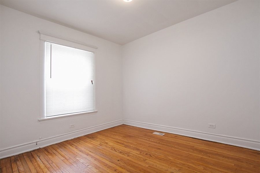 Empty room with hardwood floors, a window with blinds, and white walls.