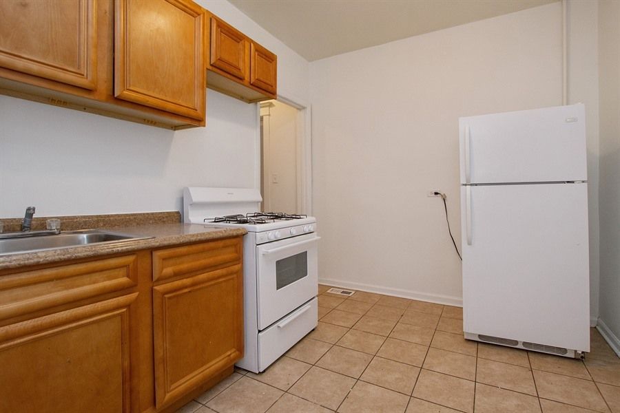Kitchen with wood cabinets, white appliances, and tan tile floor.