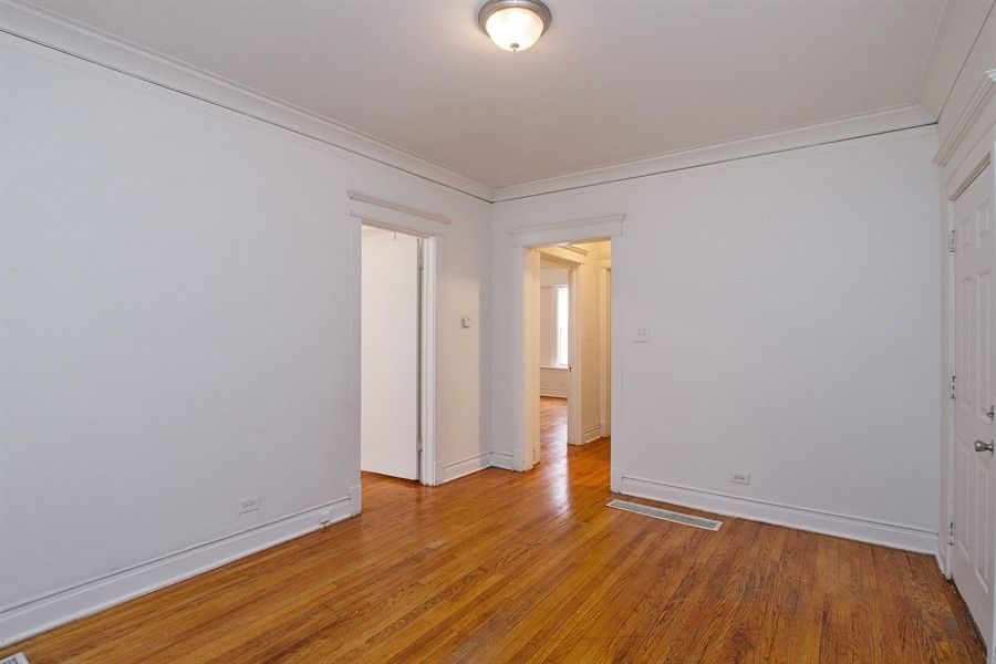 Empty room with hardwood floors, white walls, and doorways leading to other rooms.