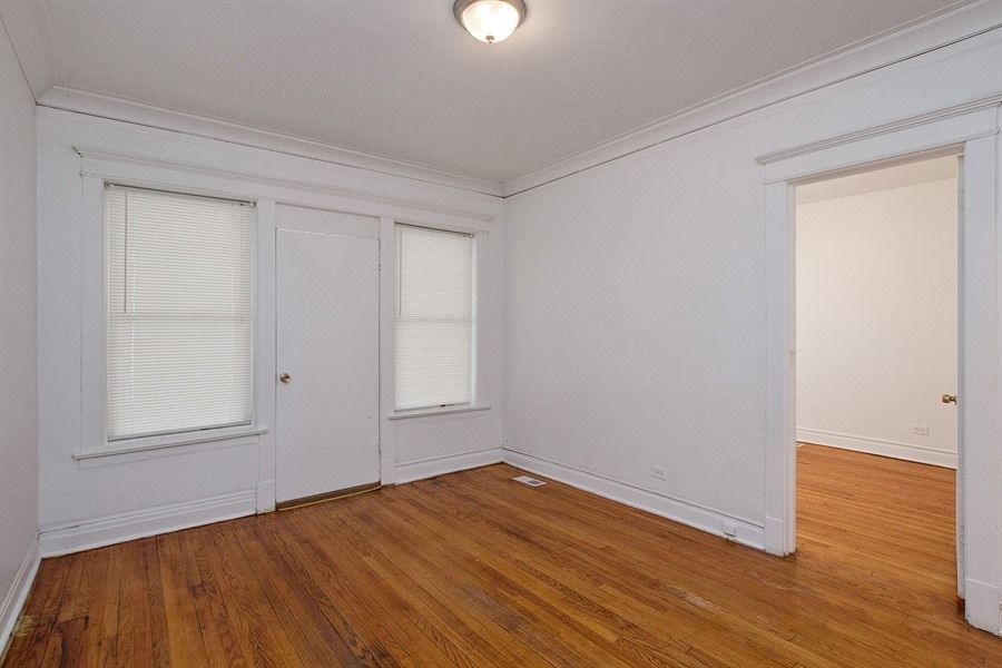 Empty room with hardwood floors, white walls, two windows, door, and overhead light.