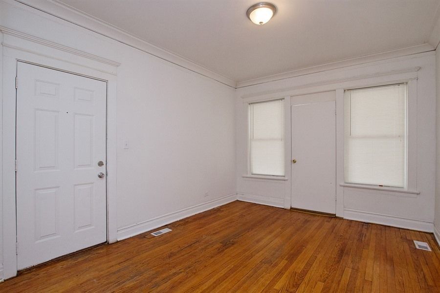 Empty room with hardwood floors, white walls, and two windows with blinds.