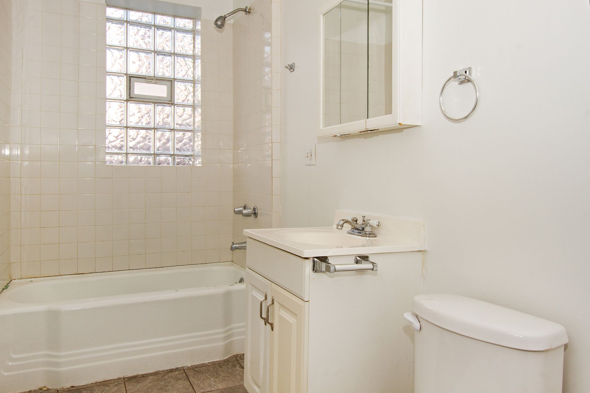 White bathroom with a bathtub, sink, toilet, and a window with glass bricks.