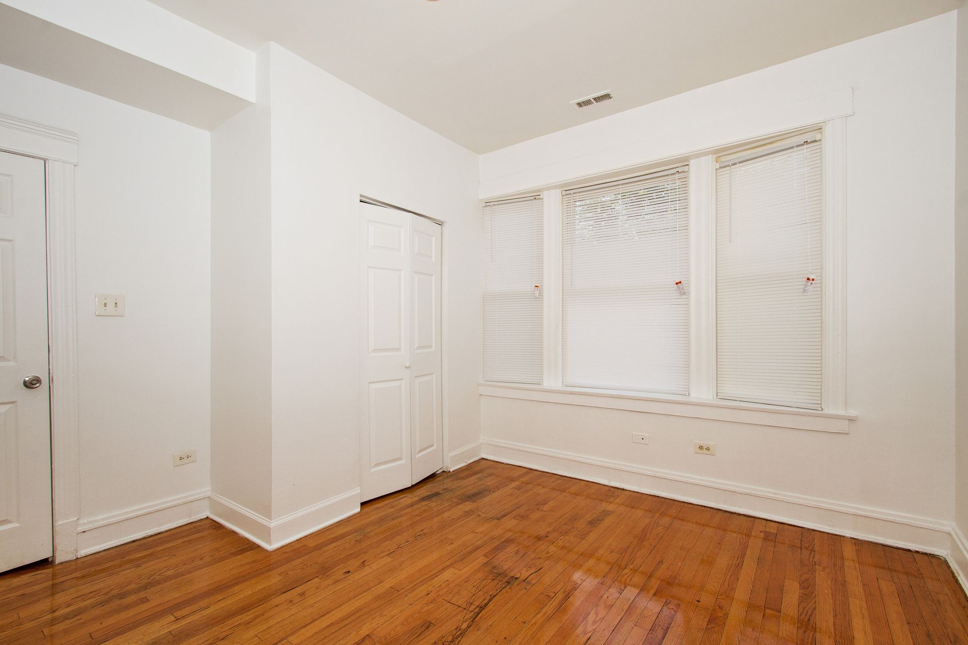 Empty room with hardwood floors, white walls, and a window with blinds.
