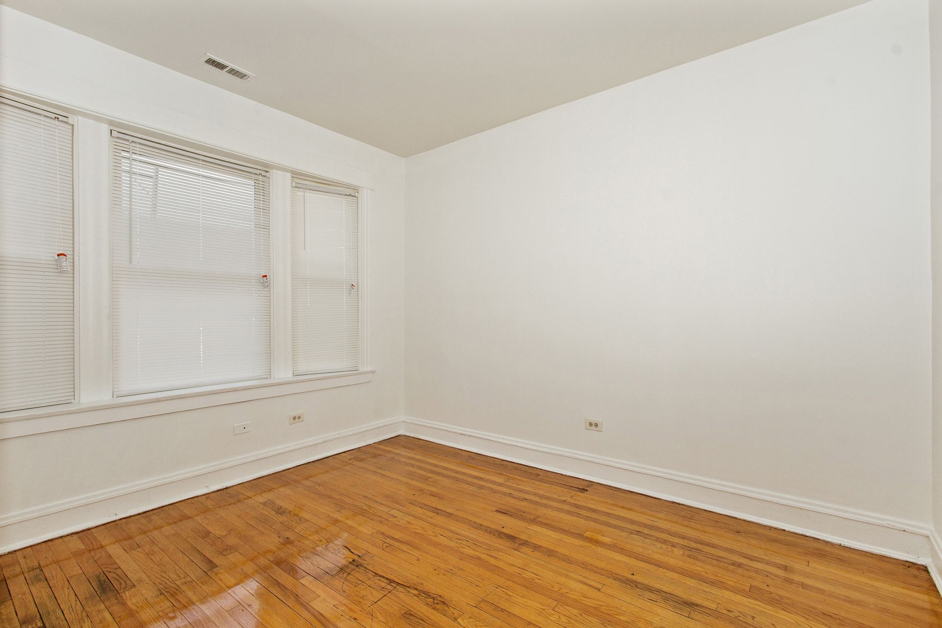 Empty room with hardwood floors, white walls, and a window with blinds.