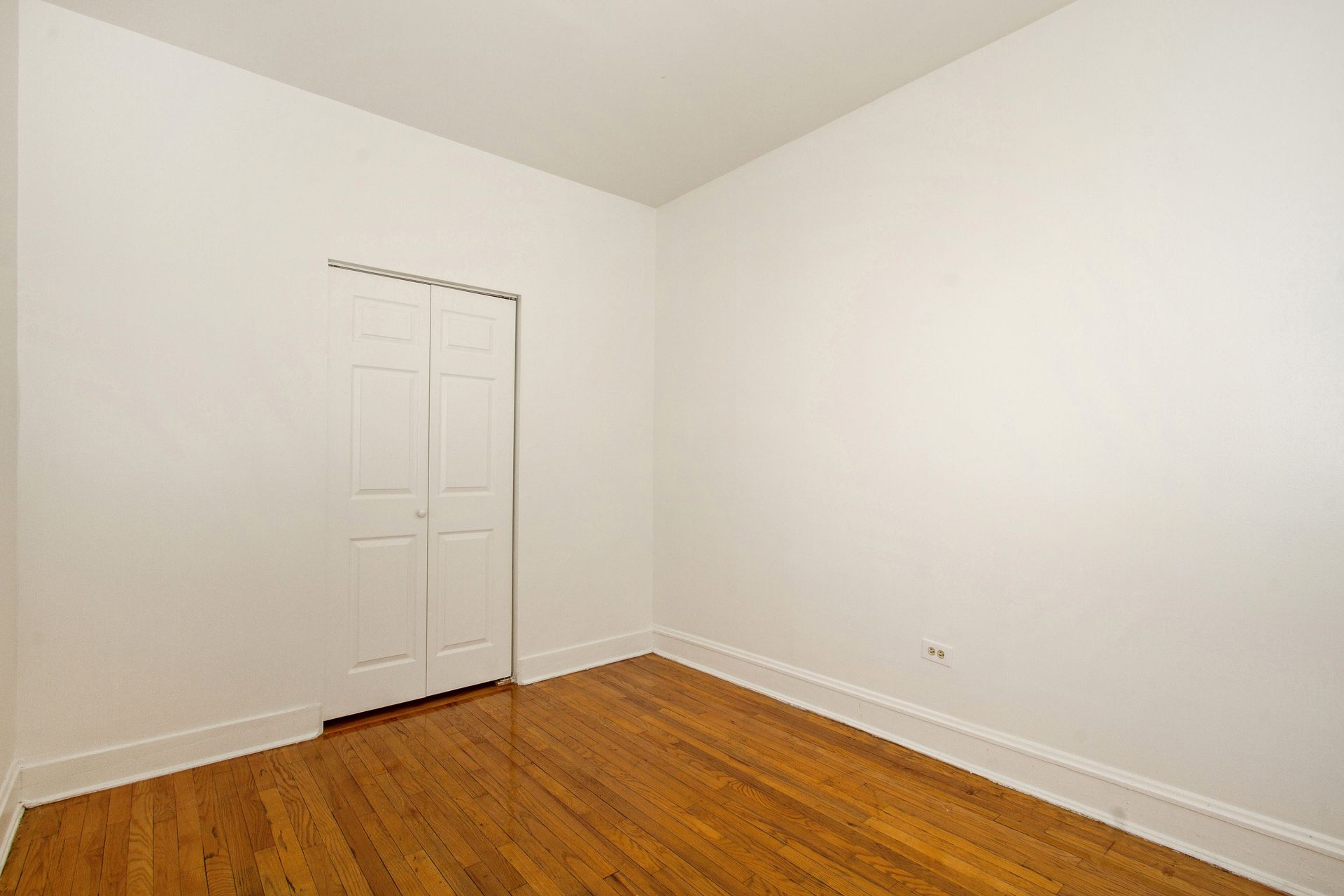 Empty room with hardwood floors, white walls, and a closet.