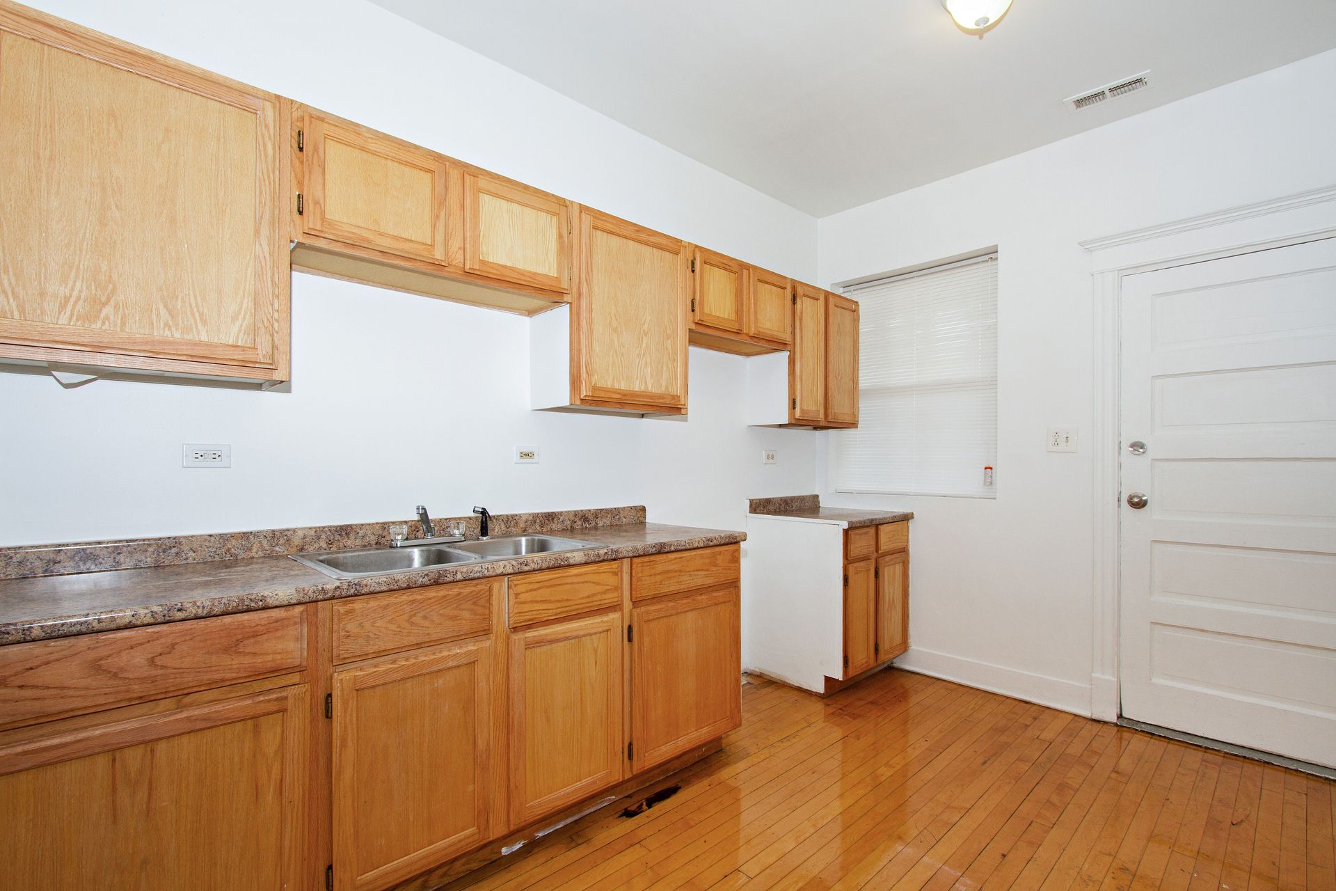 Kitchen with light wood cabinets, speckled countertop, and hardwood floor.