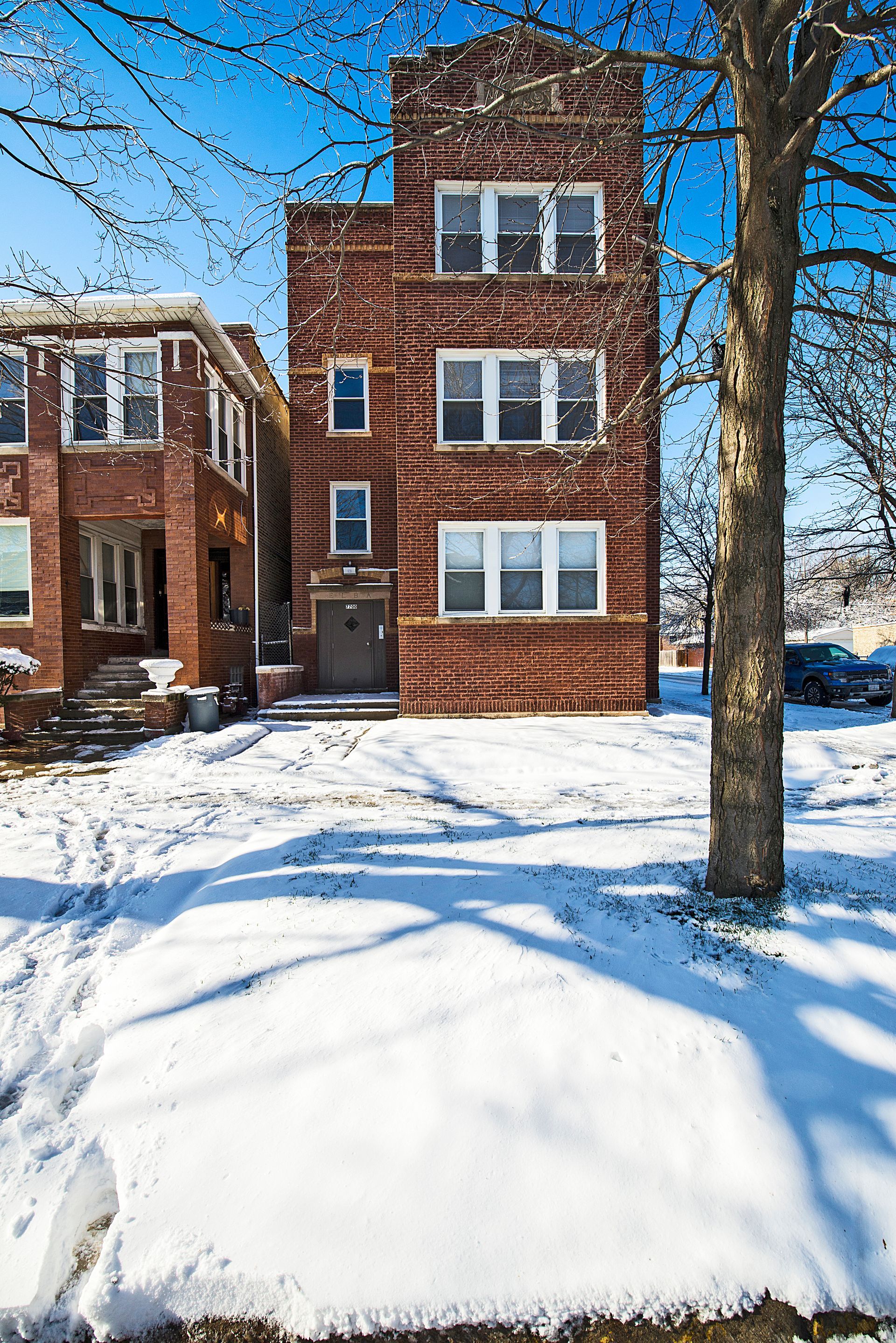 Three-story brick building in snow, next to a tree. Blue sky.
