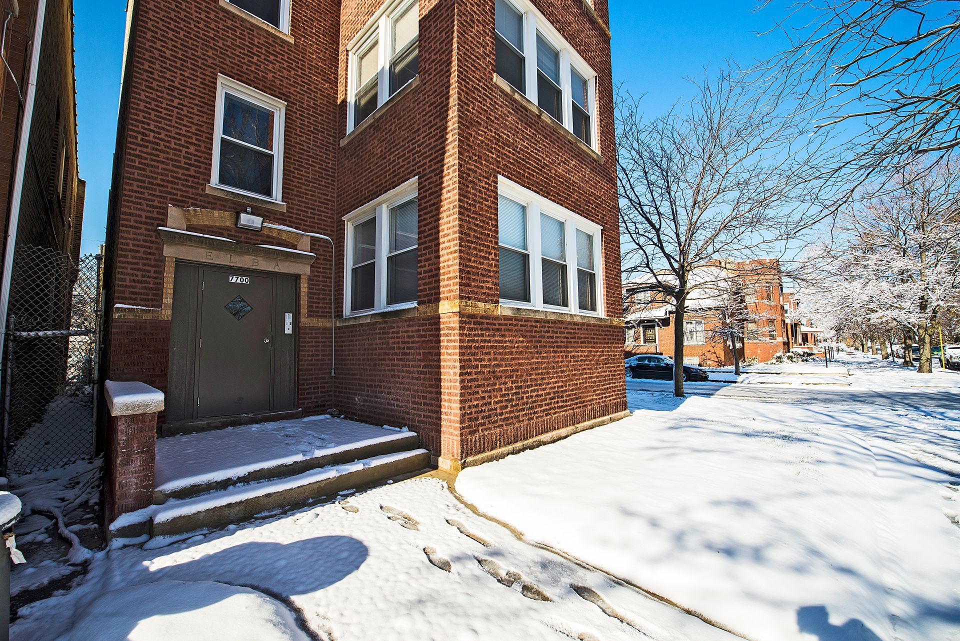 Brick building corner with steps and snow-covered ground; sunny day.