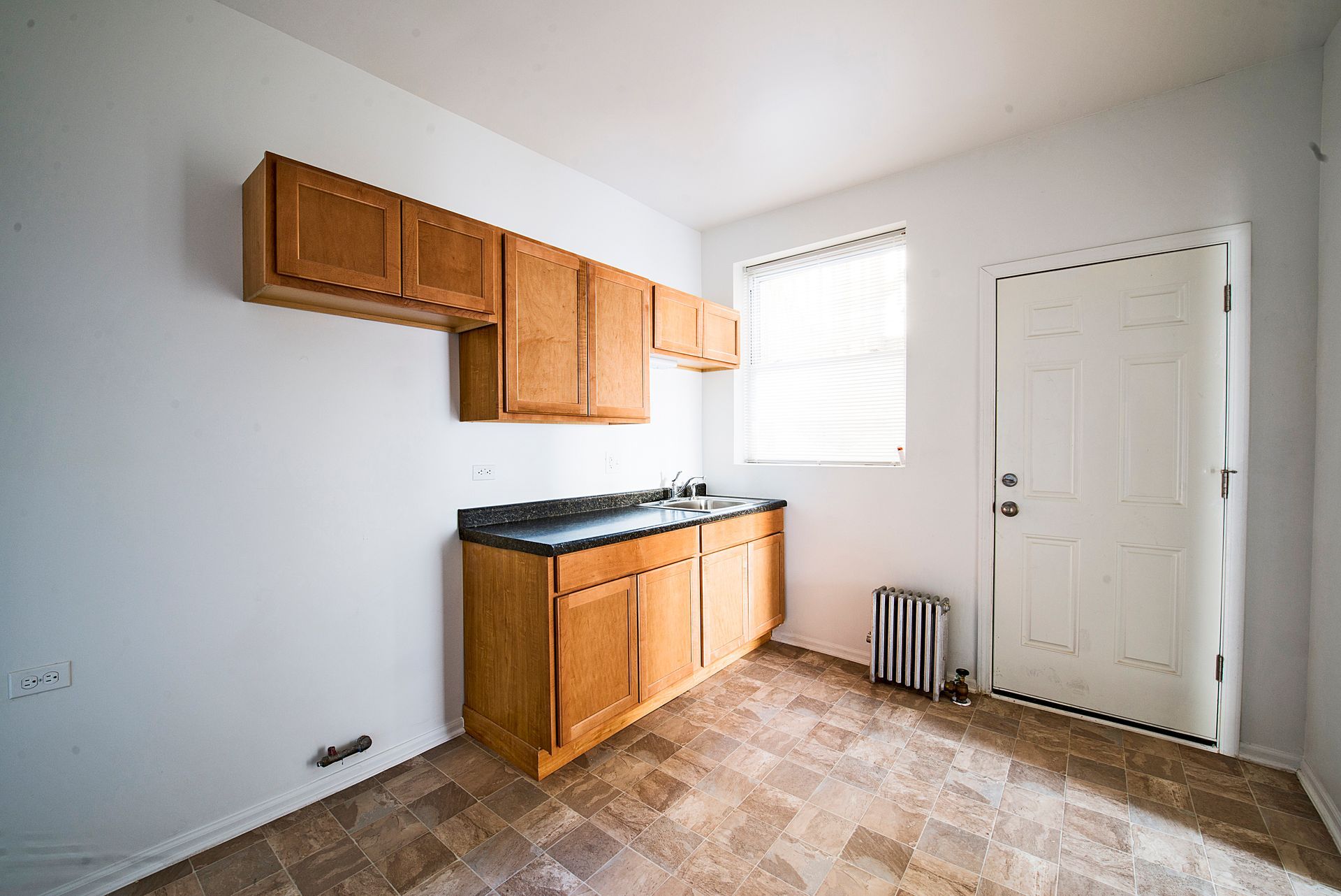 Empty kitchen with wooden cabinets, countertop, window, and door.