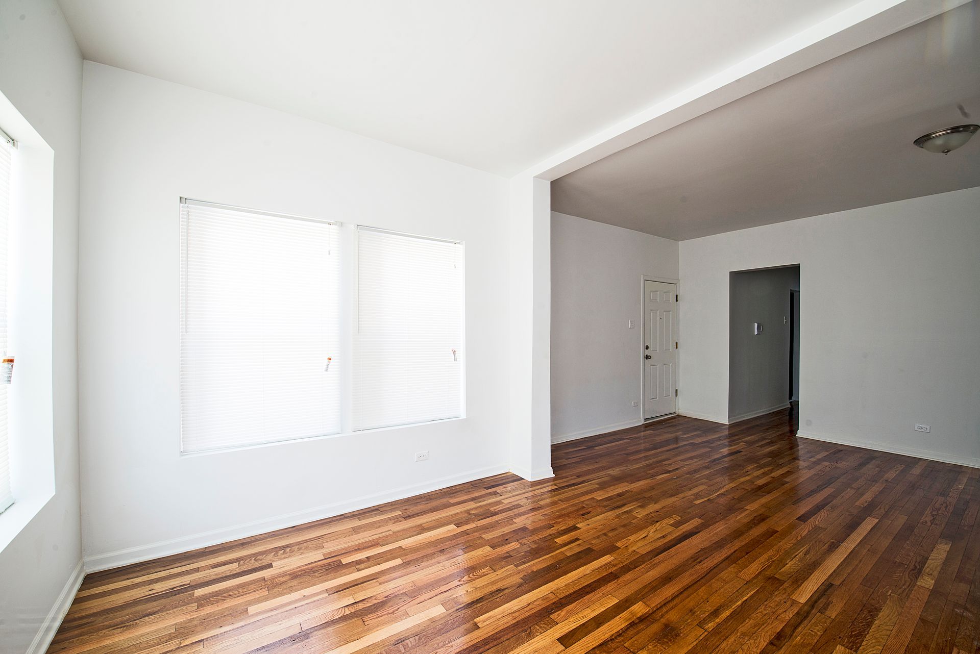 Empty room with hardwood floors, white walls, and bright sunlight.
