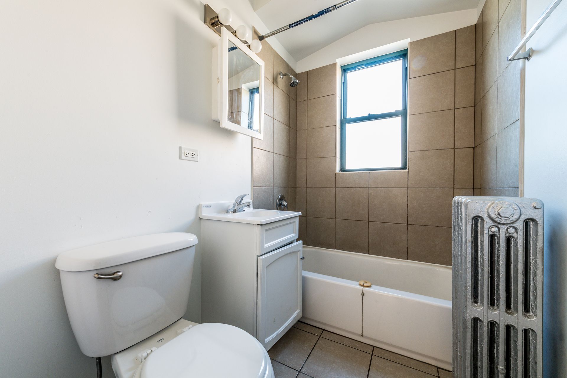 Small bathroom with a toilet, sink, bathtub, window, and radiator.
