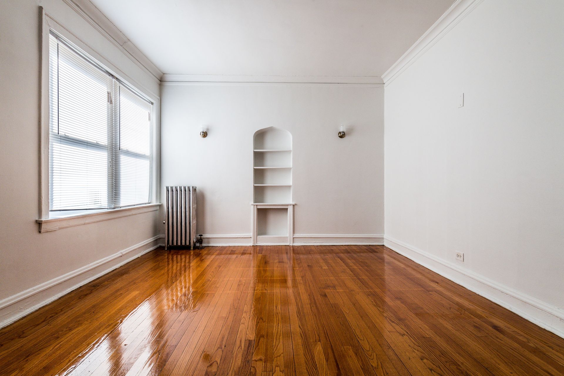 Empty room with glossy hardwood floors, built-in shelving, and a window.