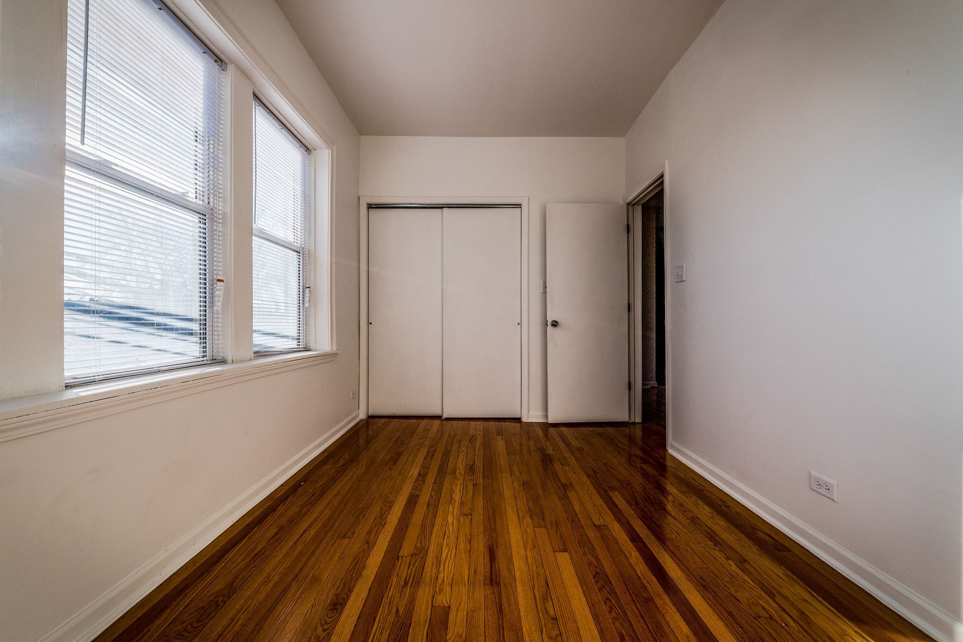 Empty room with wood floors, a window, closet, and a doorway.