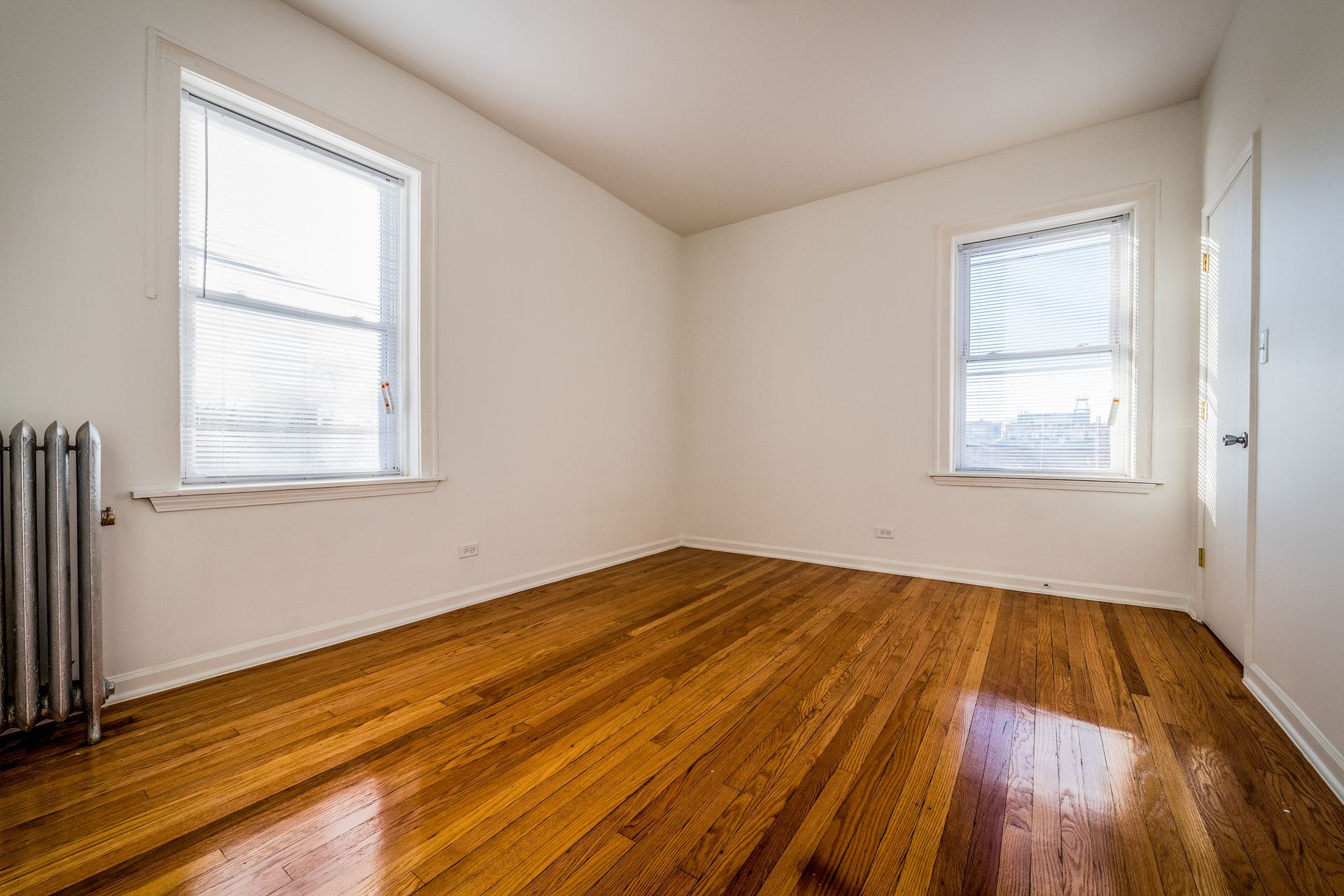 Empty room with hardwood floors, two windows, and a radiator.