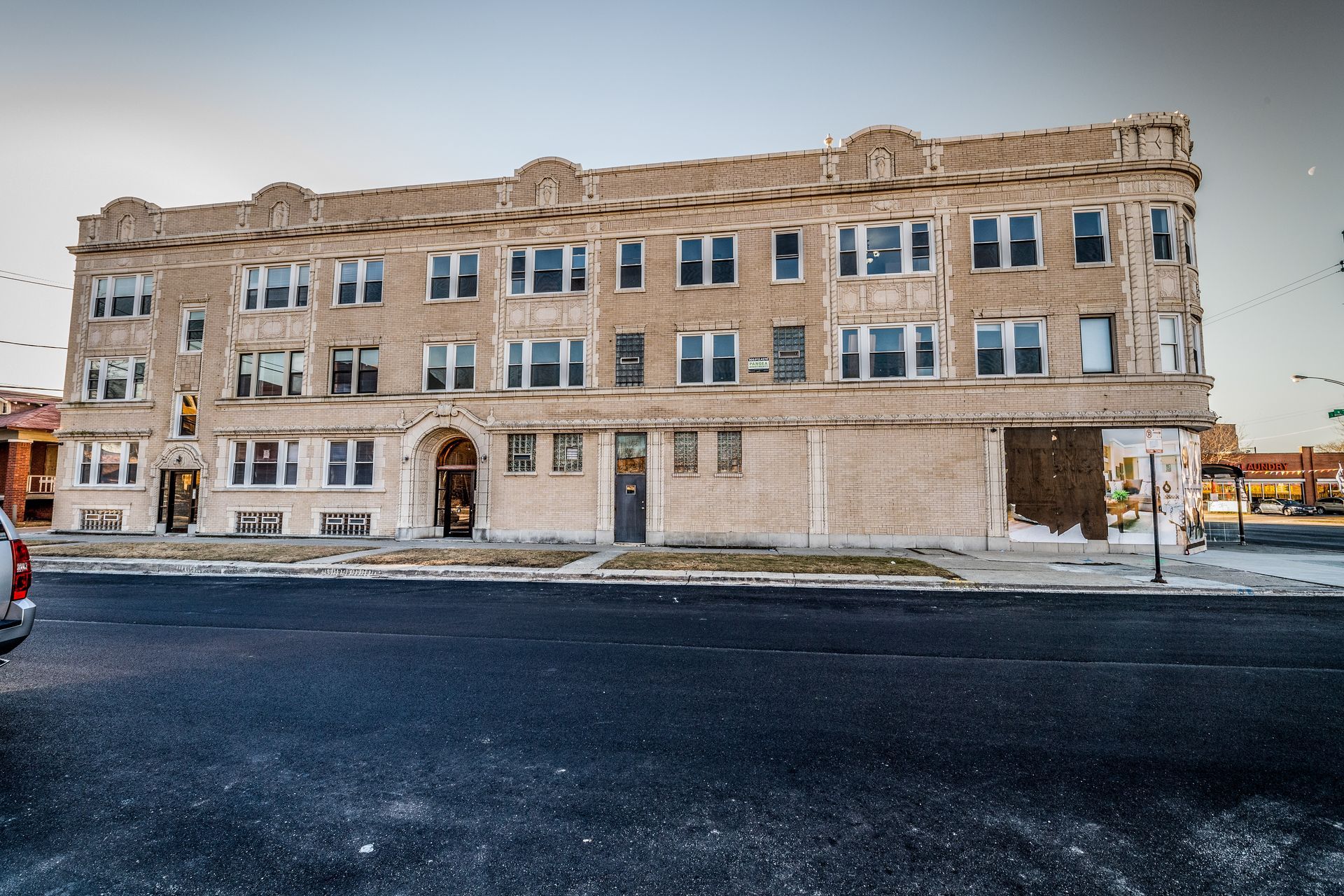 Three-story beige brick building with multiple windows; dark asphalt street in front.
