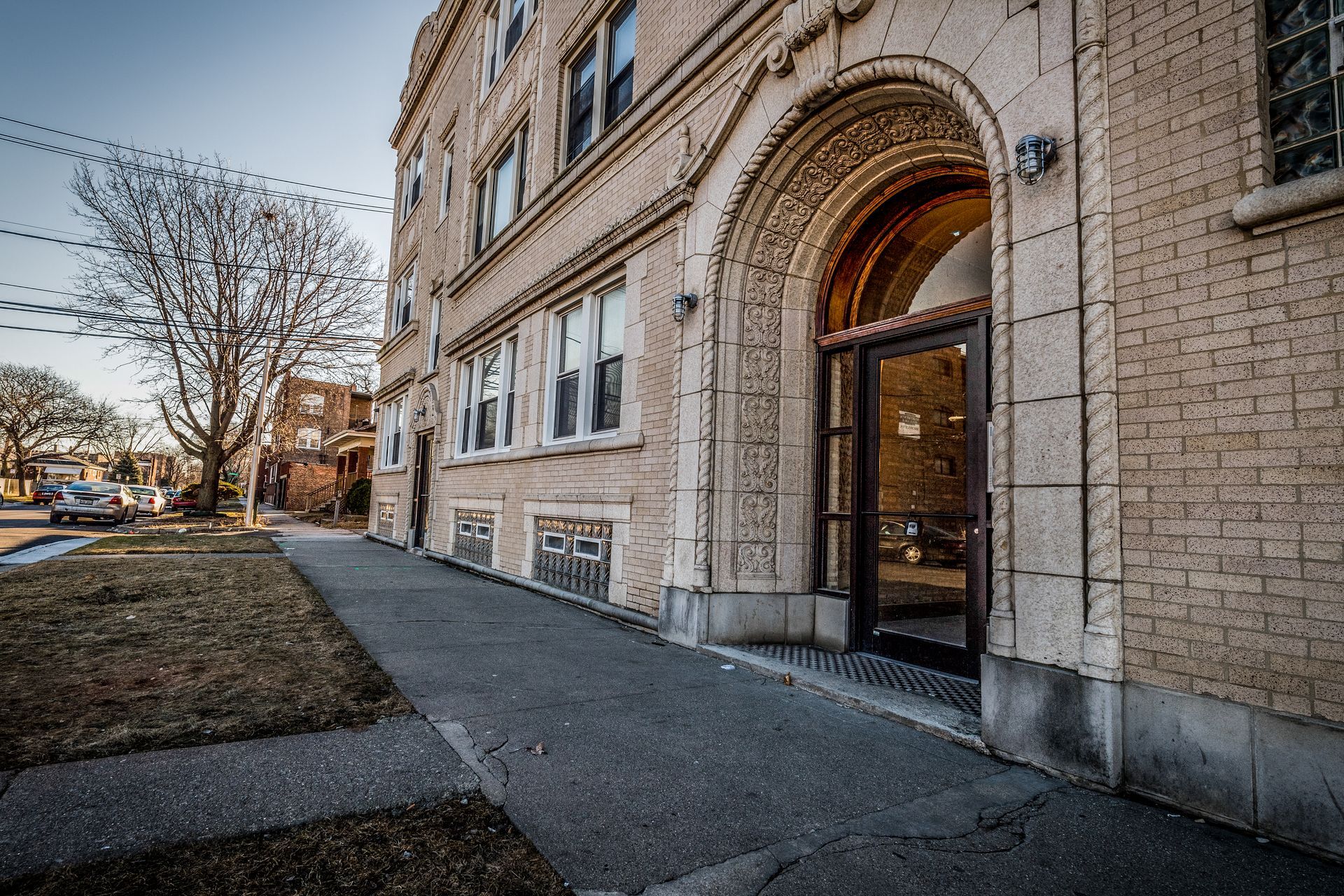 Exterior of beige brick apartment building with arched entrance and sidewalk ramp.