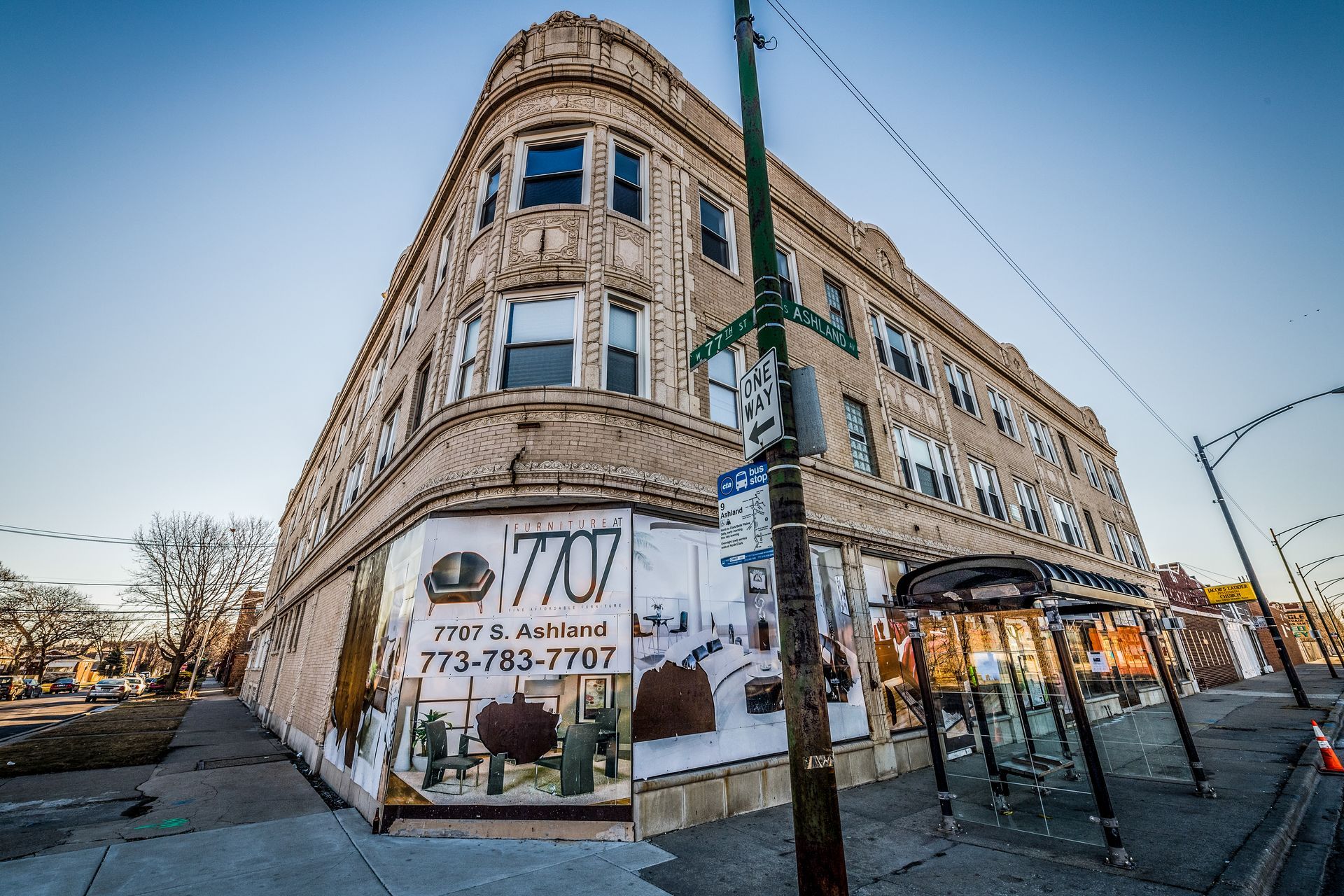 Corner building with painted storefront, three stories, light-colored brick facade. Street and bus stop visible.