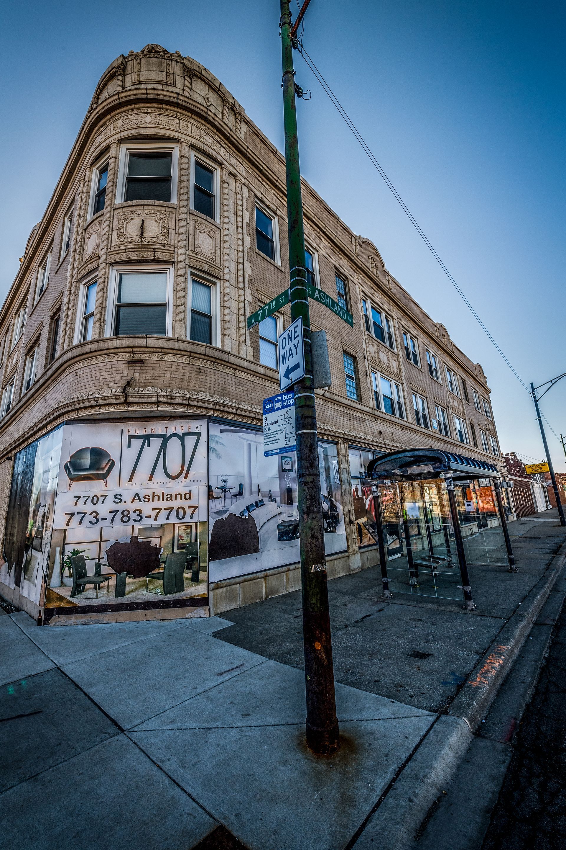 Corner building with store mural and bus shelter along a sidewalk under a clear blue sky.