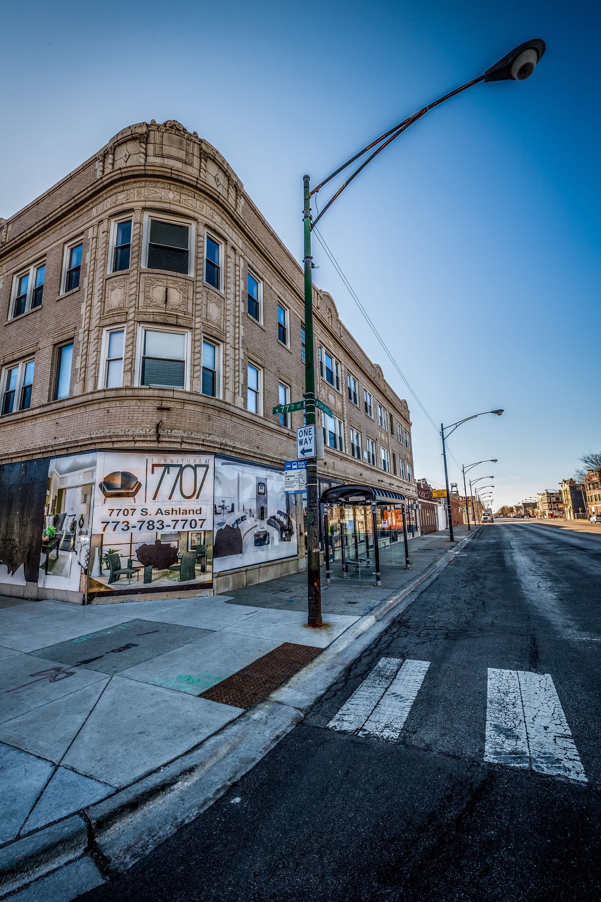 Building on a corner with a shop at street level, crosswalk, and lamppost on a sunny day.