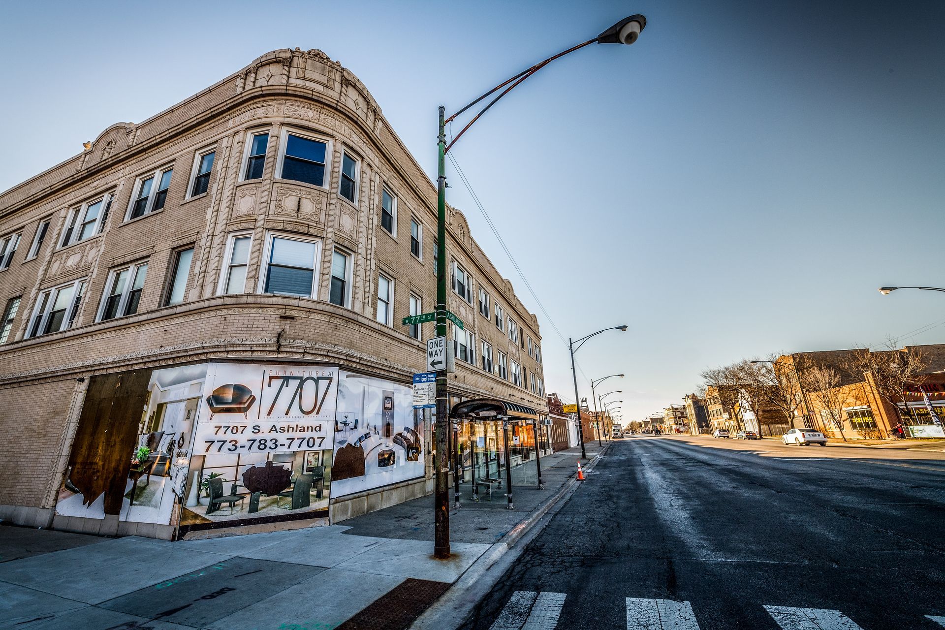 Street view of a three-story building with a corner shop, on a sunny day.
