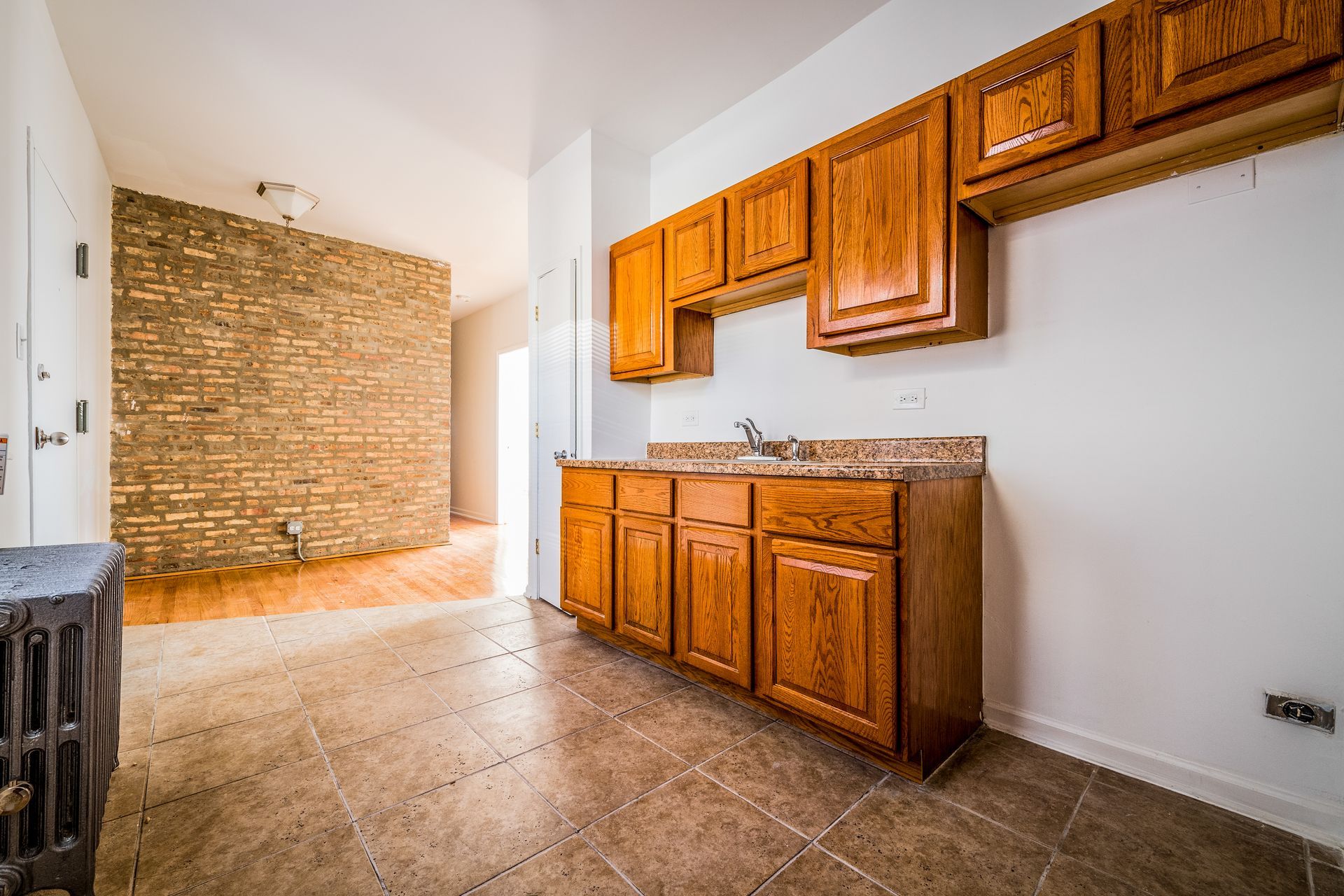 Kitchen with wooden cabinets, a sink, and a tiled floor. A brick wall is visible in the background.
