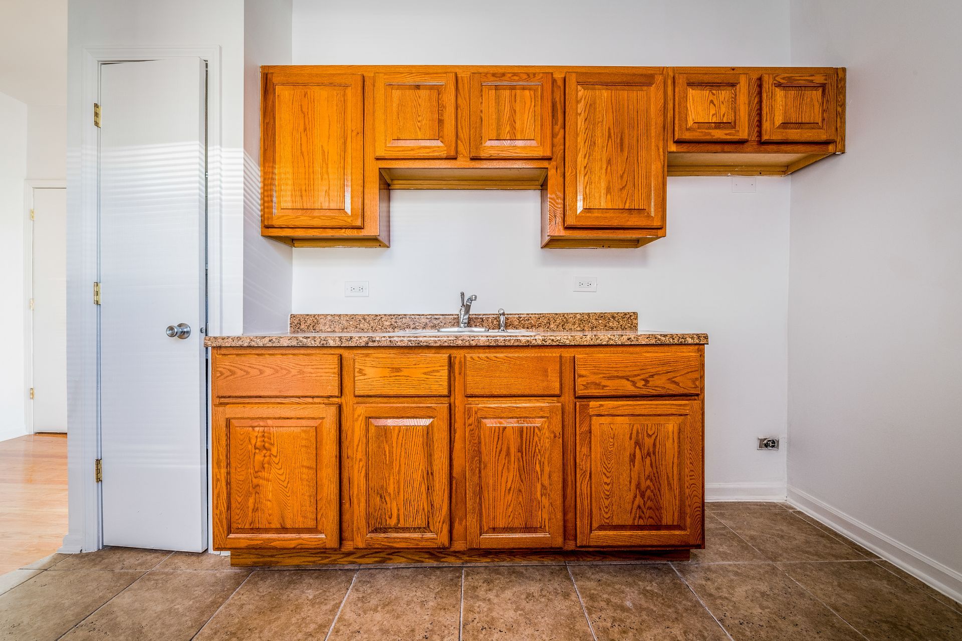 Wooden kitchen cabinets mounted on a white wall. Countertop and sink are installed. A door is visible.