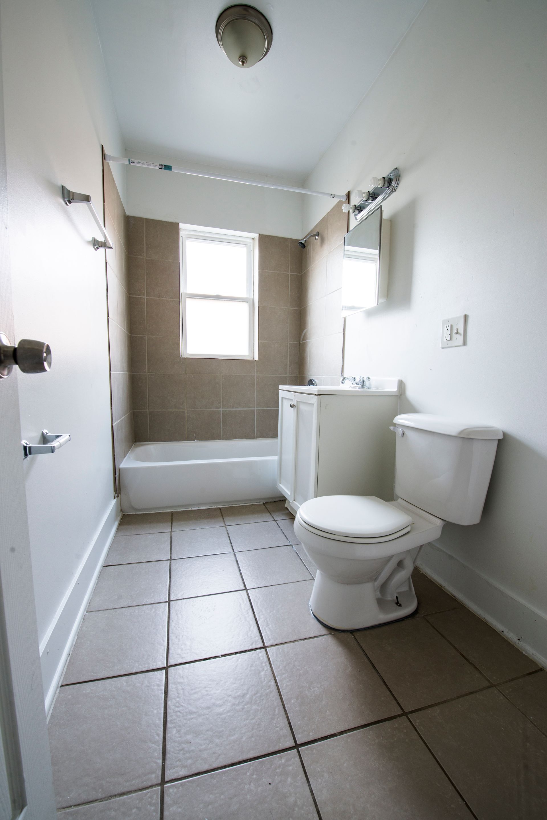 Bathroom with a white toilet, sink, and tub. Beige tiled floor and wall accents.