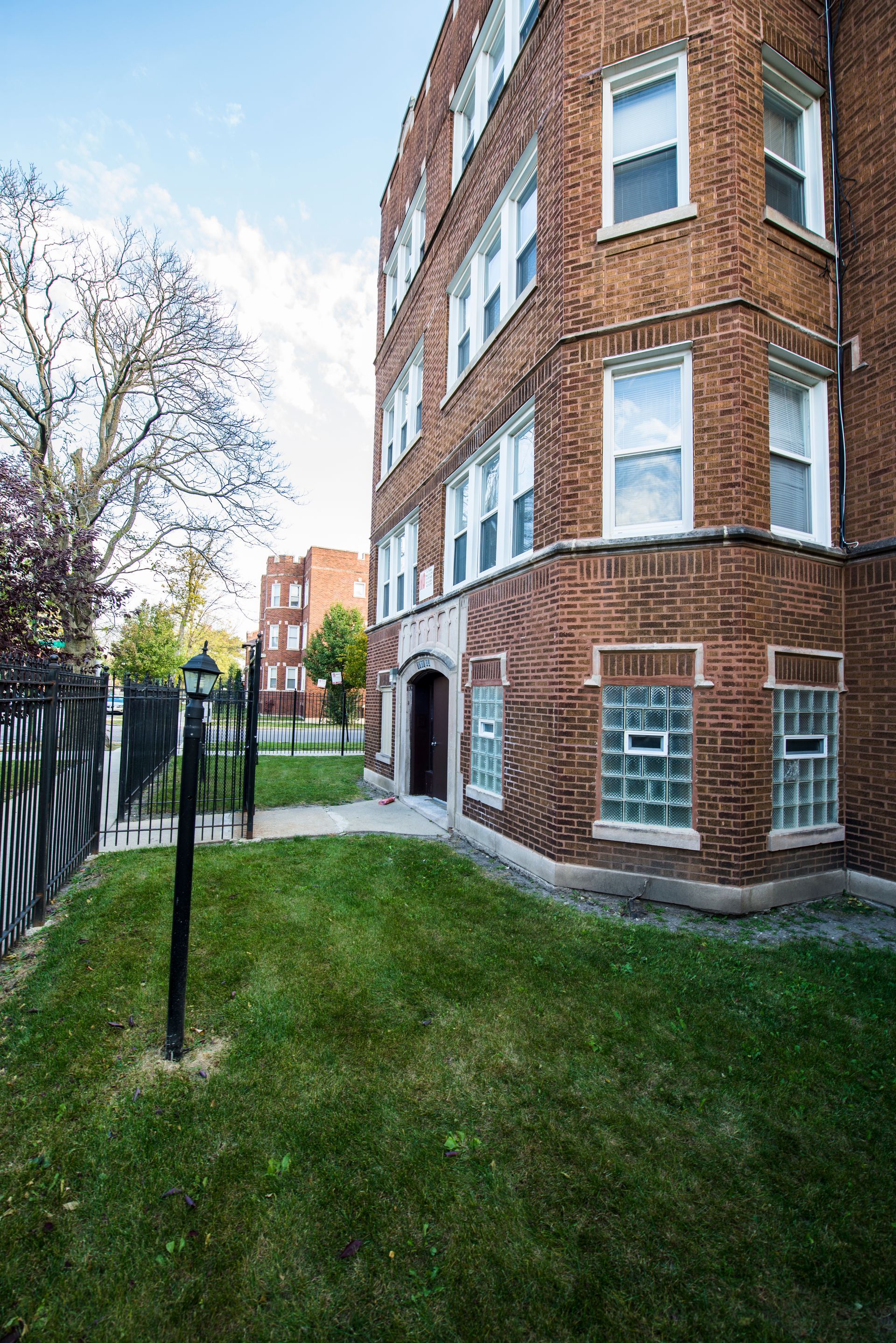 Brick apartment building with green lawn, glass block windows, and a black fence.