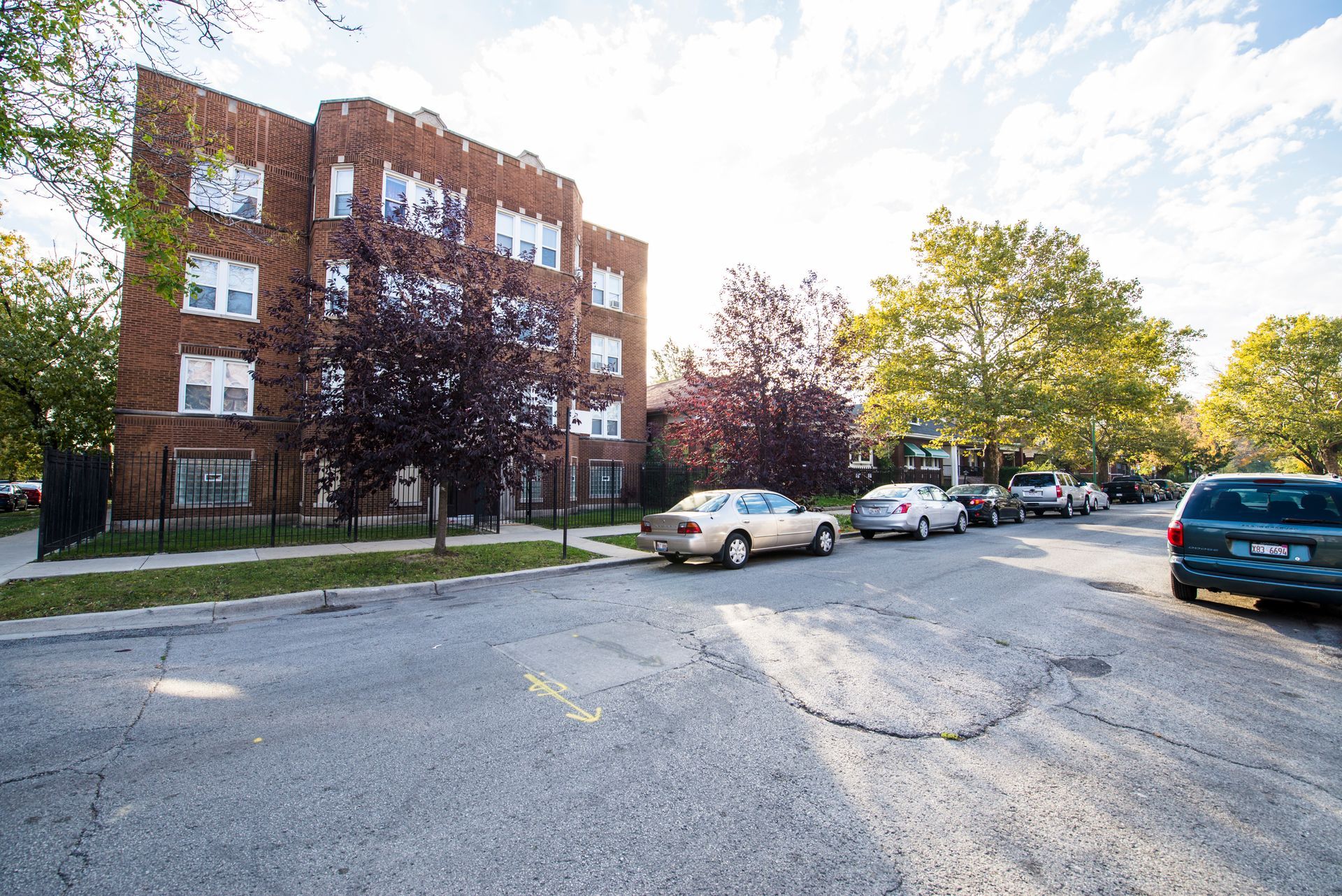 Brick apartment building on a street with parked cars and trees.