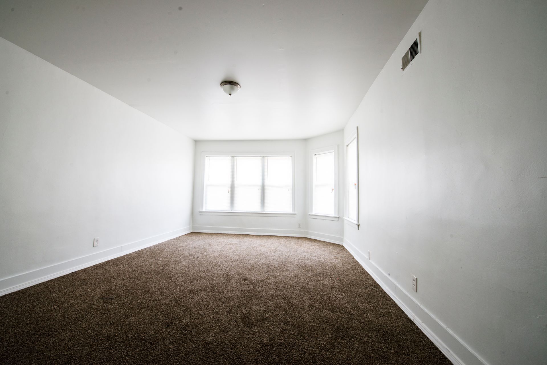 Empty room with brown carpet, white walls, and a large window.